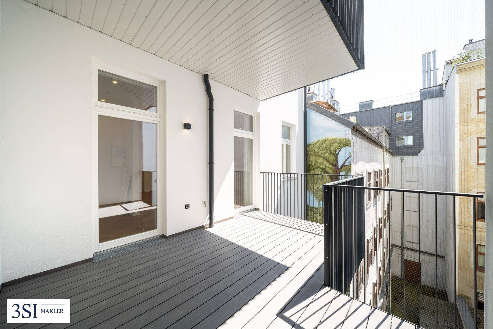 Geräumiger Balkon mit Holzdielenboden und schwarzem Geländer, bietet Platz im Freien.