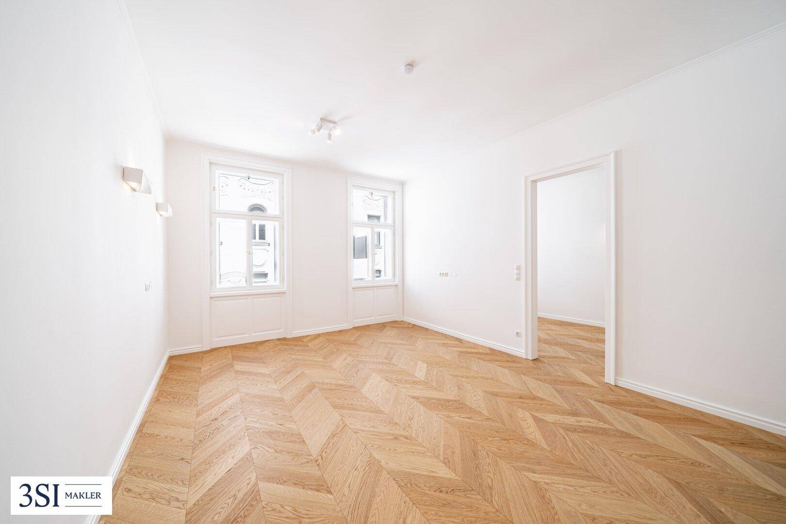 Heller Raum mit Fischgrätparkett und zwei großen Fenstern, ideal für Wohn- oder Schlafzimmer.
