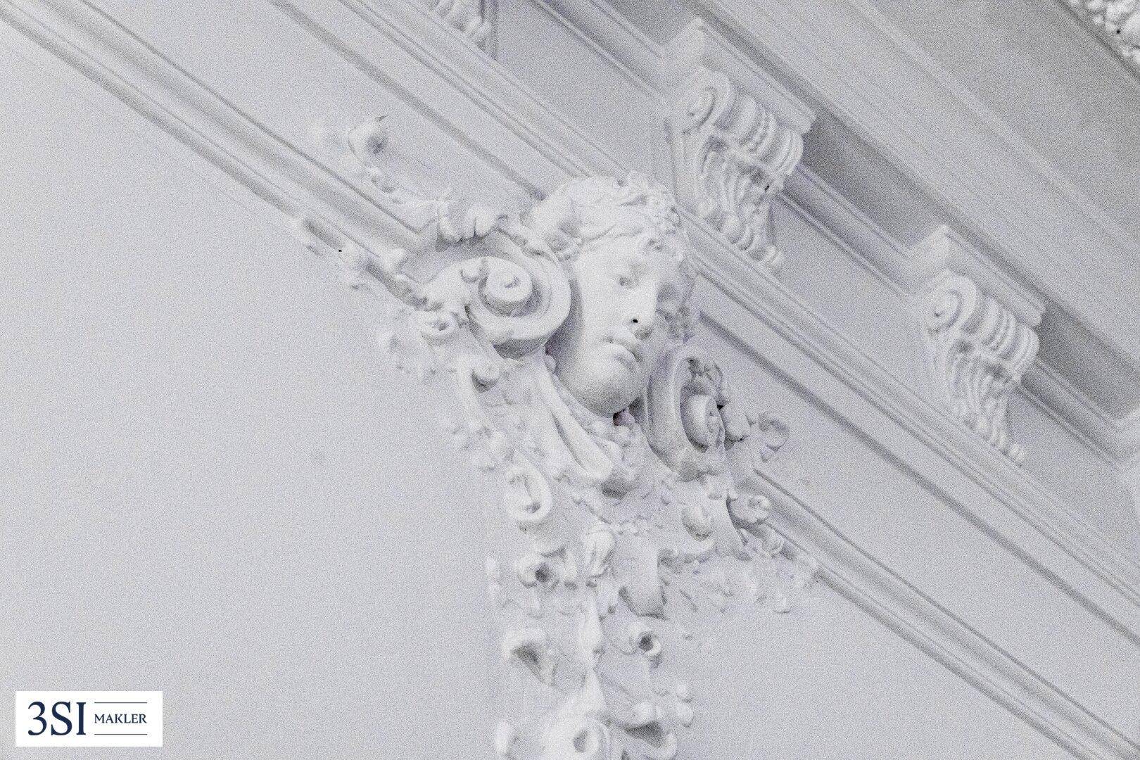 Nahaufnahme einer kunstvollen Stuckverzierung an der Wand eines historischen Gebäudes.