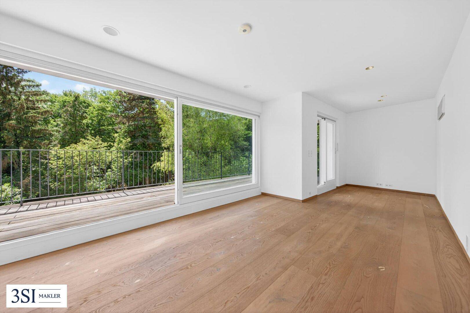 Helles Zimmer mit Holzboden, großen Fenstern und Zugang zu einem breiten Balkon.