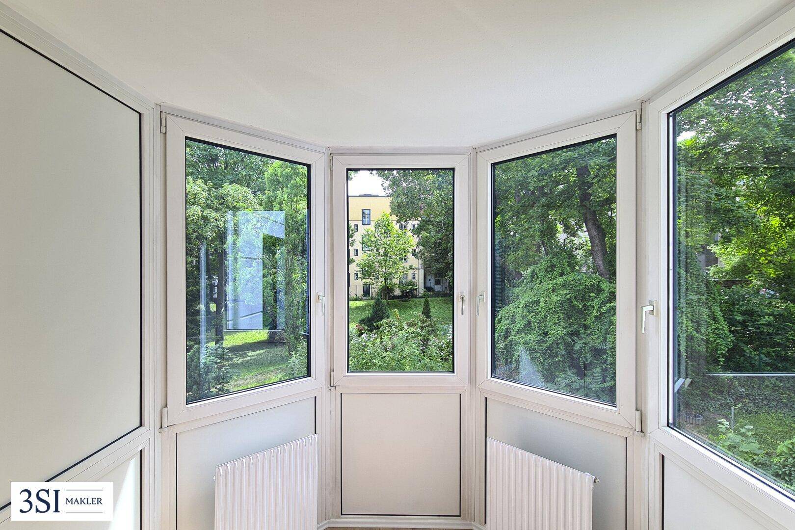 Heller Erkerbereich mit großen Fenstern und einem schönen Blick auf den grünen Innenhof.