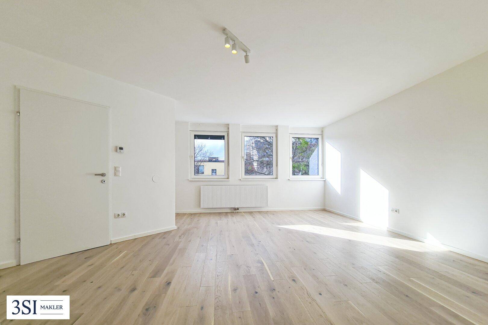 Heller Raum mit modernem Holzboden, weißen Wänden und drei Fenstern für viel Tageslicht.