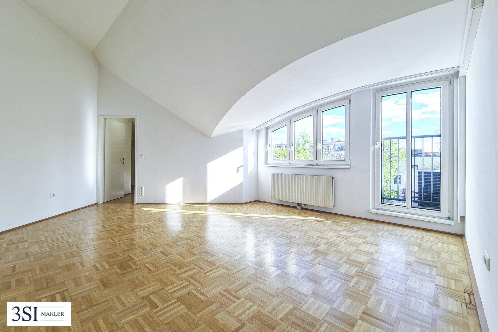 Helles Zimmer mit Parkettboden, Dachschrägen und Zugang zu einem französischen Balkon.