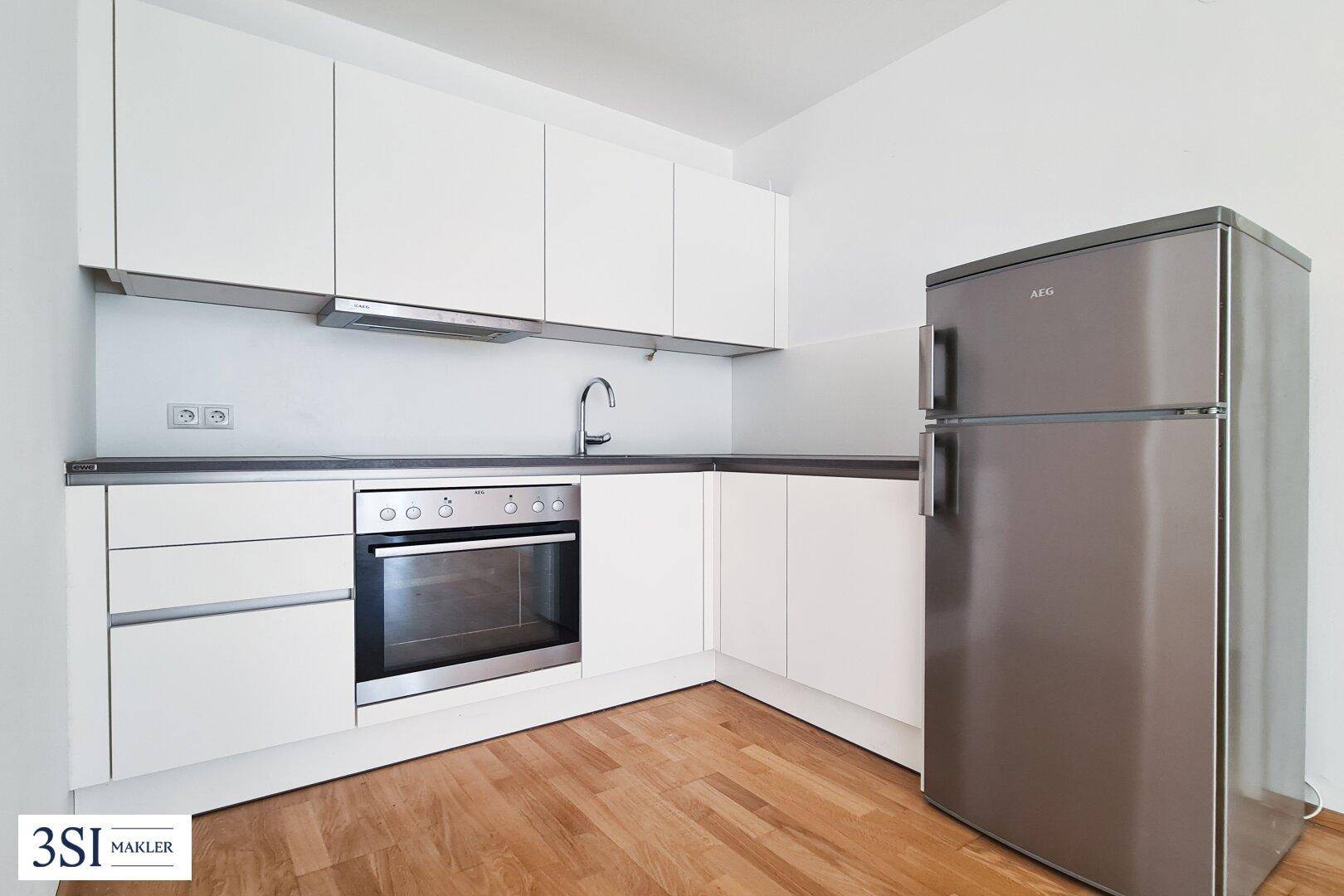 Kompakte Küche mit weißen Schränken, integriertem Backofen, Gaskochfeld und freistehendem Kühlschrank.