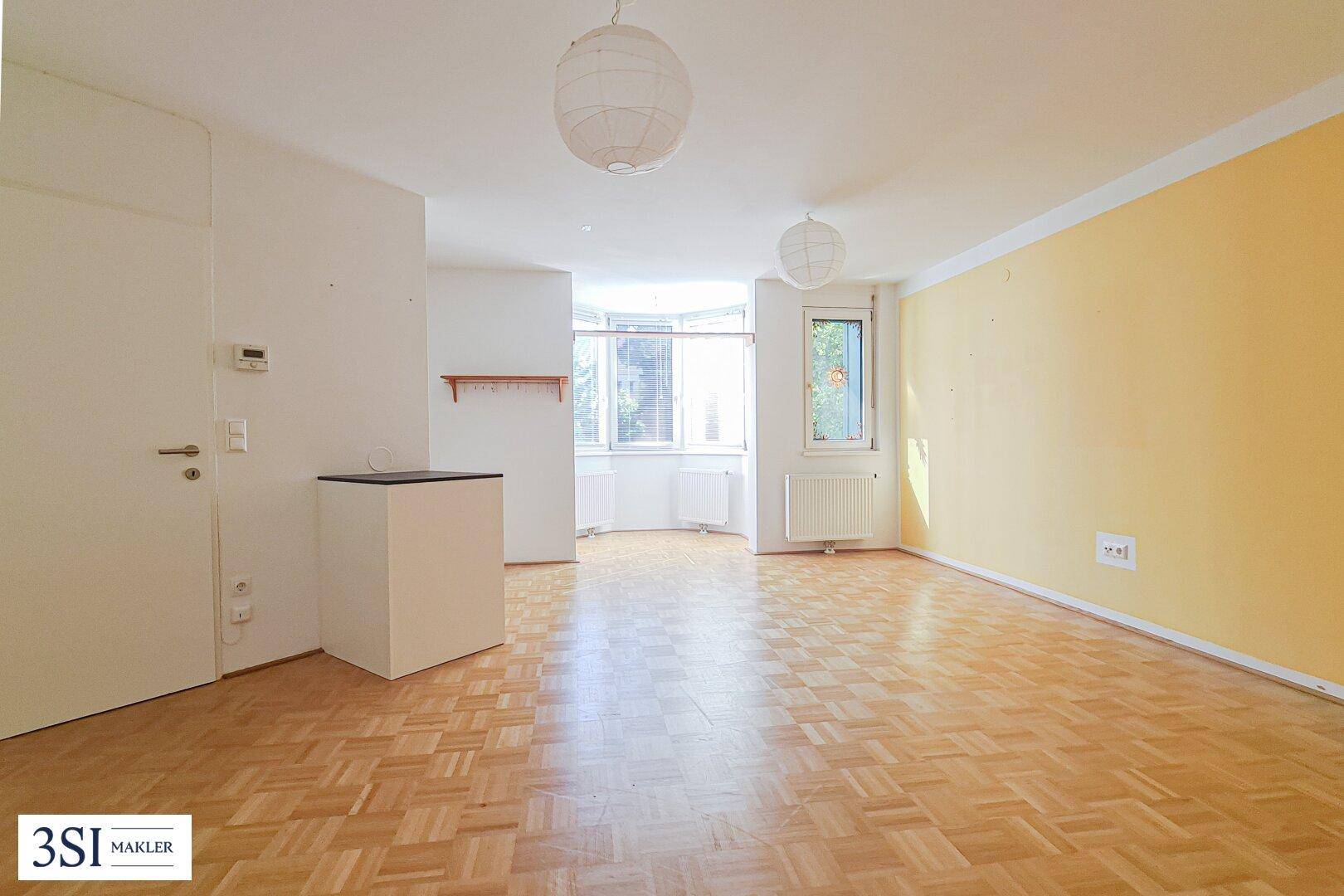Geräumiges Zimmer mit Parkettboden, gelber Akzentwand und einem hellen Erkerbereich.