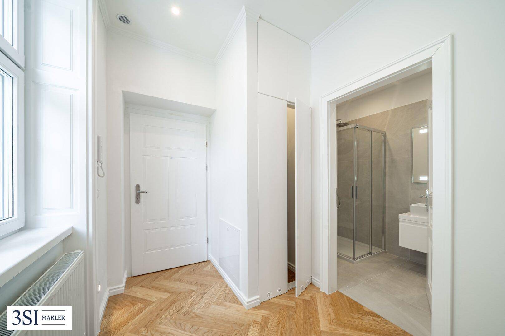Heller Flur mit Fischgrätparkett und Zugang zu einem modernen Badezimmer mit Dusche.