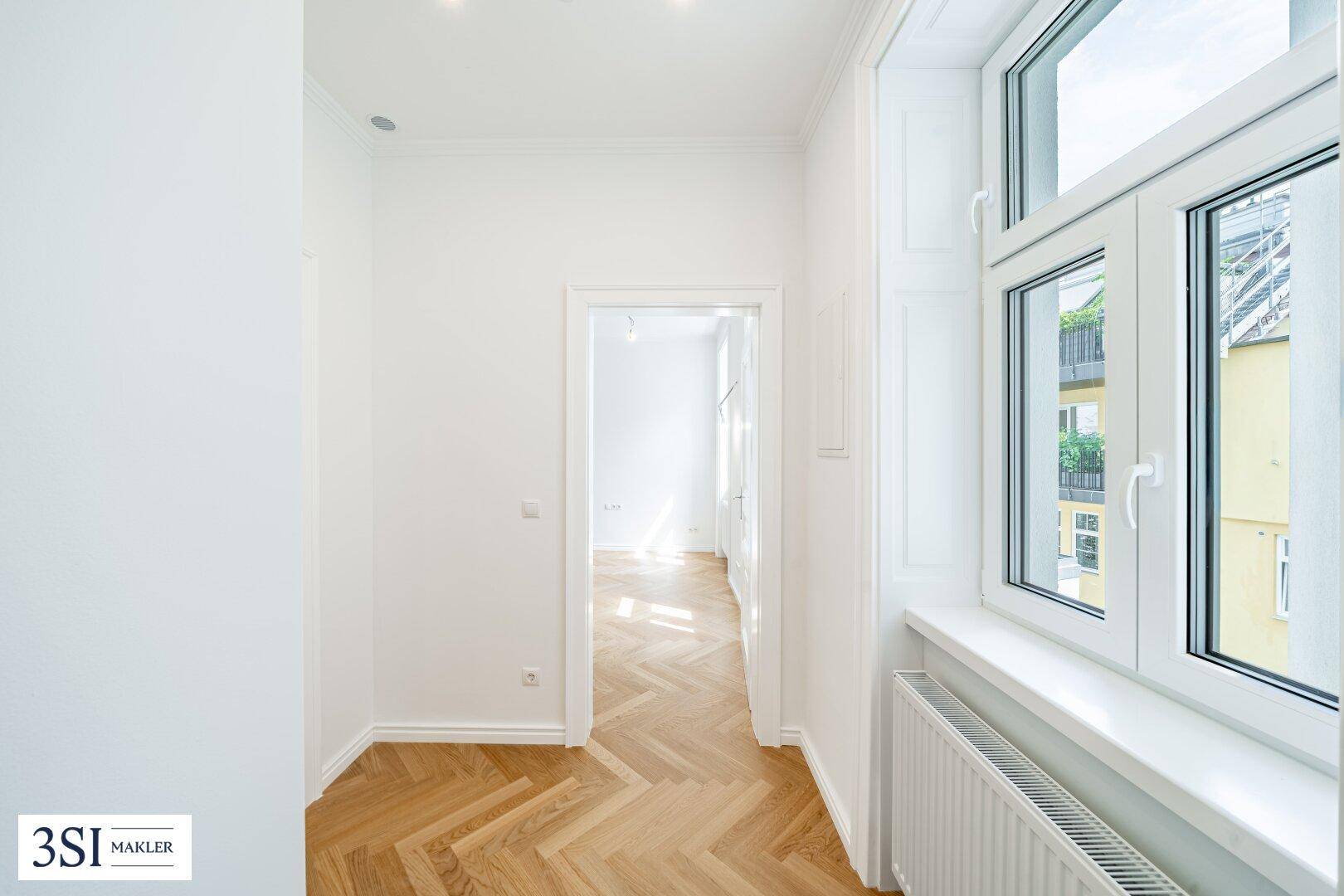 Langer, heller Flur mit klassischem Fischgrätparkett und Blick in weitere Zimmer.