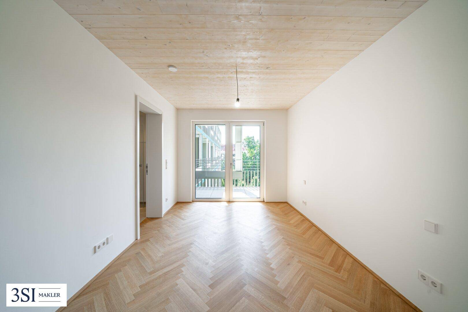 Unmöbliertes Schlafzimmer mit Fischgrätparkett, Holzbalkendecke und Zugang zu einem Balkon.