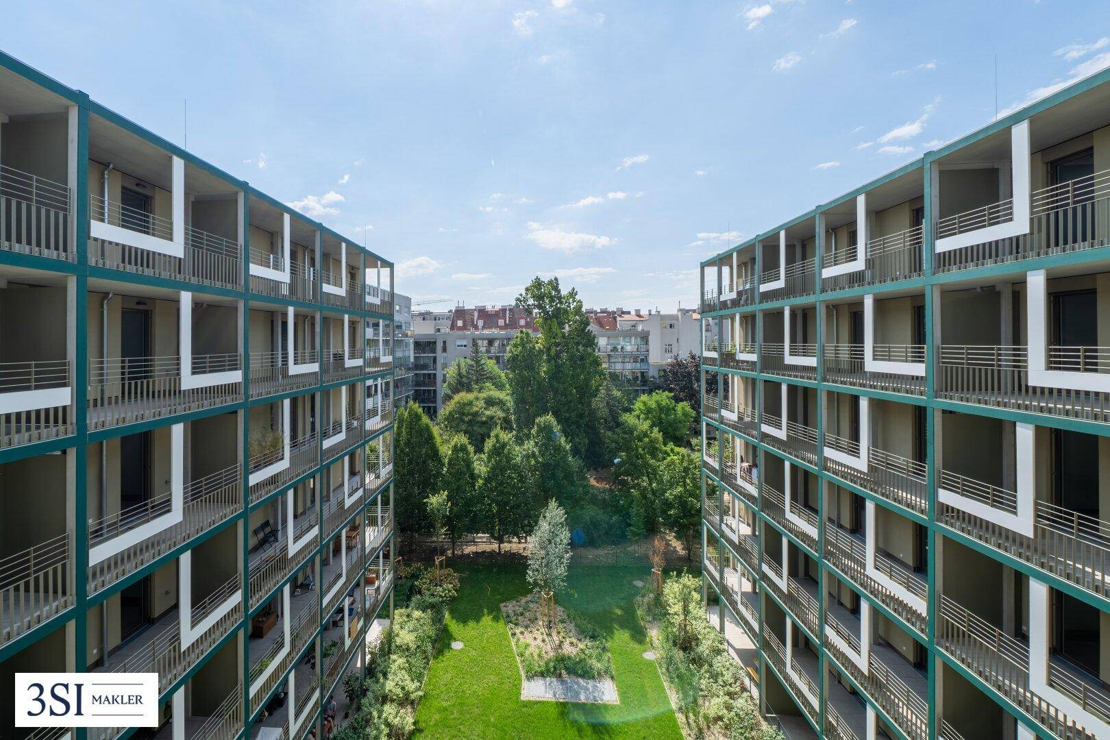 Blick auf den begrünten Innenhof zwischen modernen Wohngebäuden unter blauem Himmel.