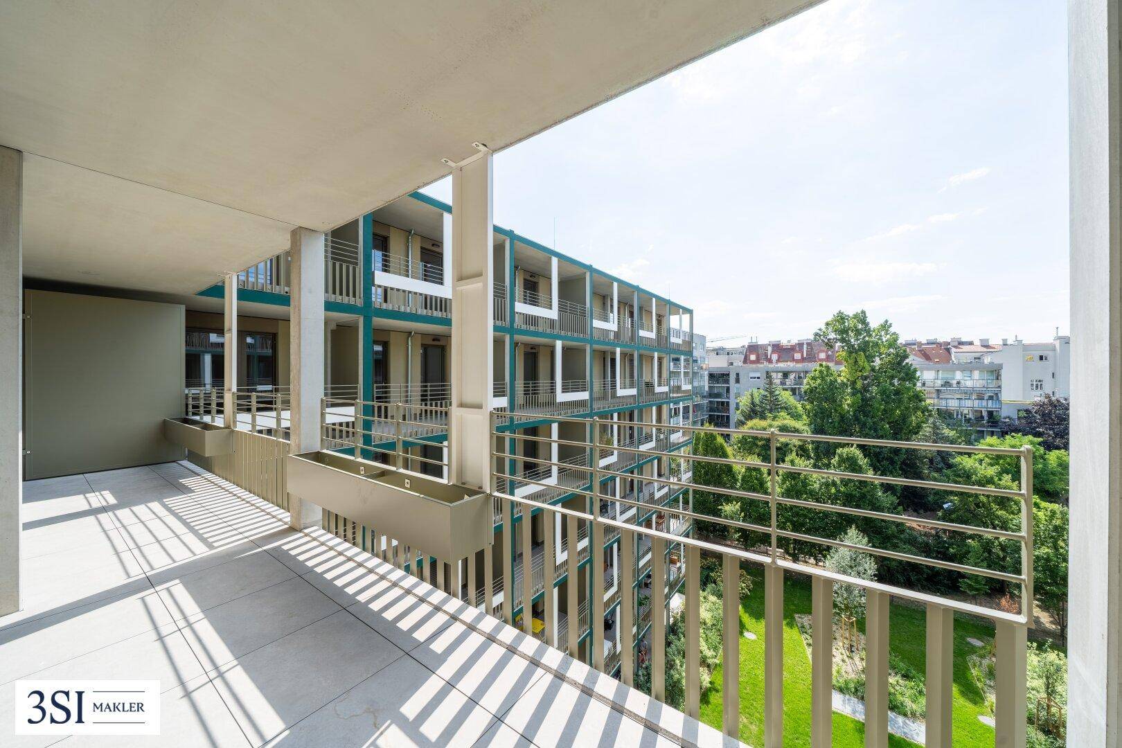 Geräumiger Balkon mit Fliesenboden und weitem Blick auf den grünen Innenhof und die Nachbargebäude.