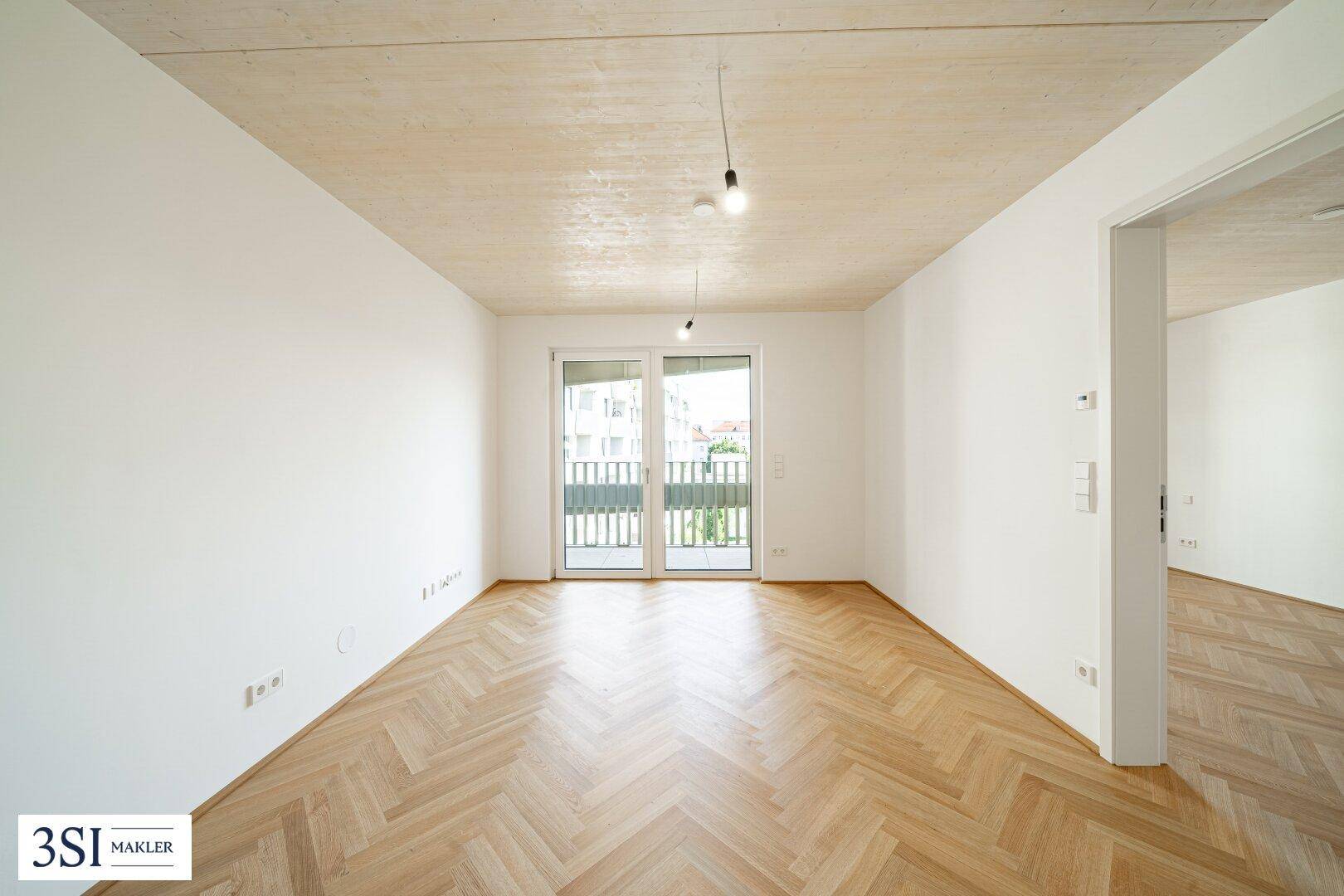 Geräumiges Zimmer mit hellem Fischgrätparkett, Holzbalkendecke und Balkonzugang.
