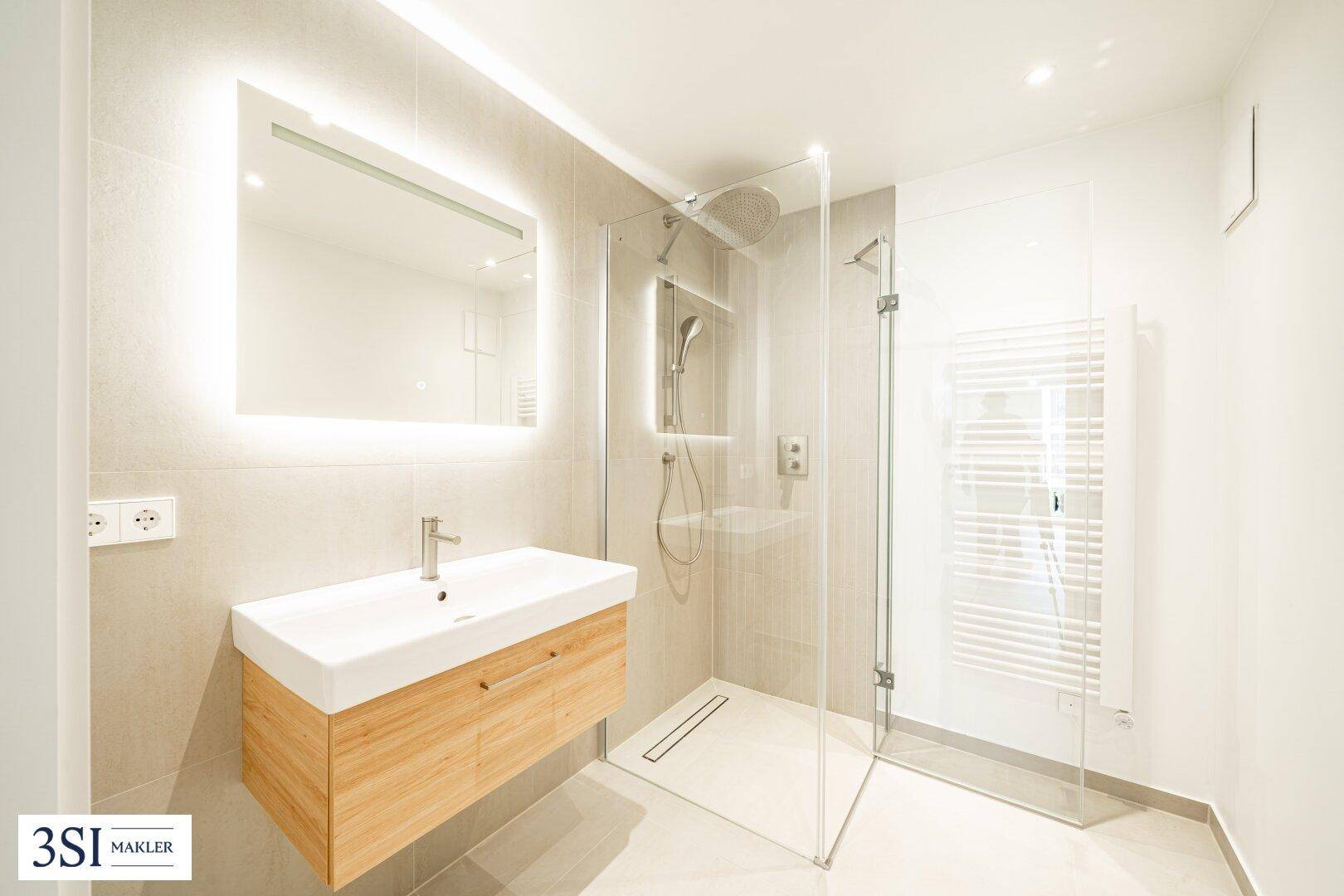 Modernes Badezimmer mit begehbarer Dusche, beleuchtetem Spiegel und stilvollem Holzwaschtisch.