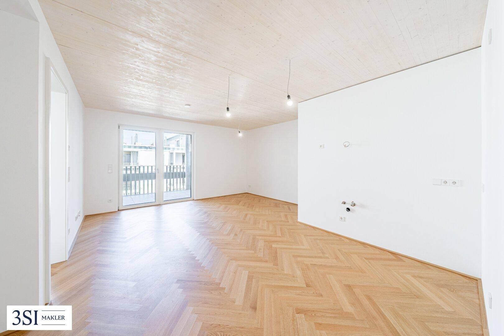 Großer, heller Raum mit Fischgrätparkett, Holzdecke und Anschlüssen für eine Küche oder Bad.