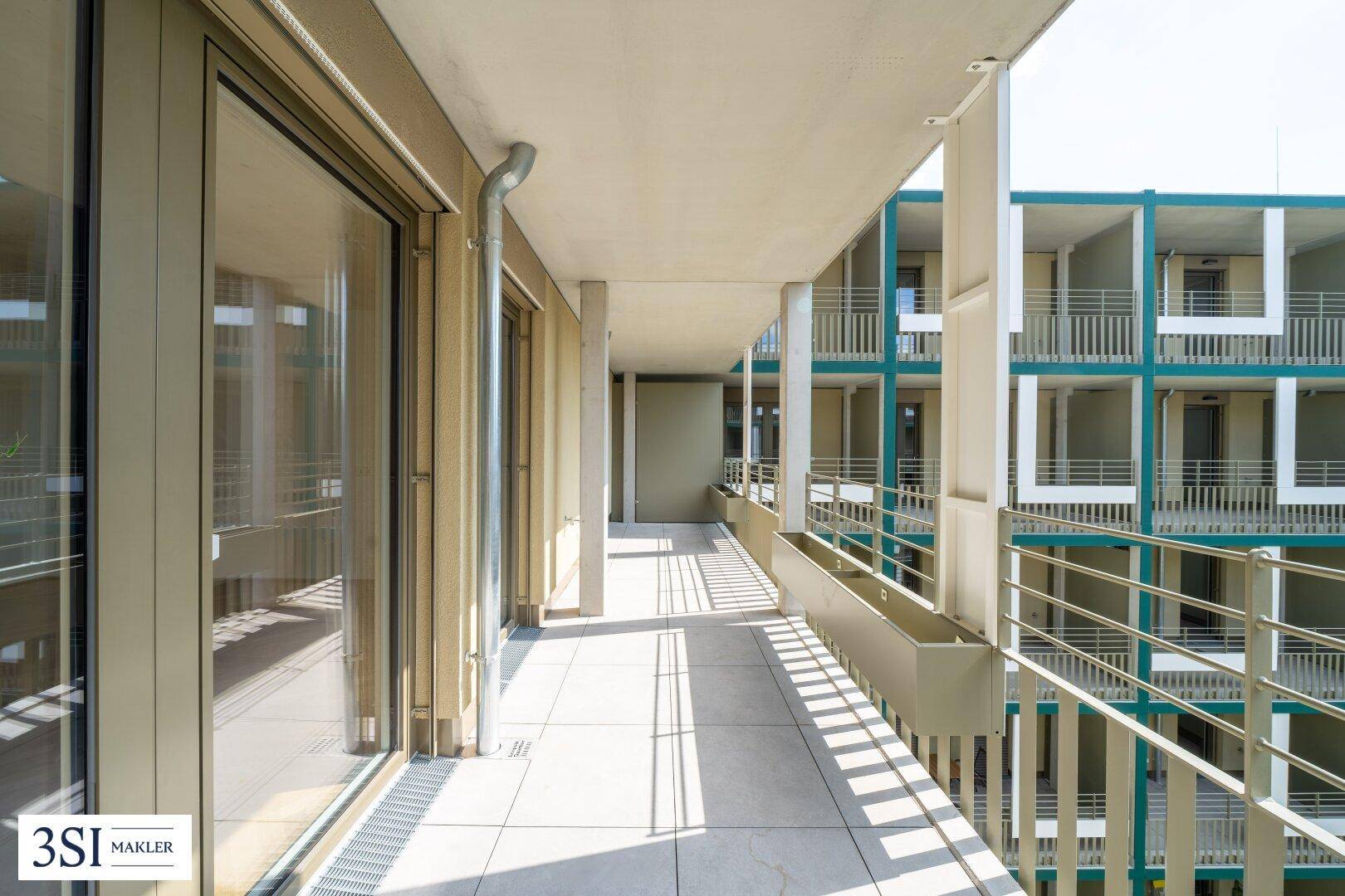 Geräumiger Balkon mit Fliesenboden und großen Glasfronten, bietet Zugang zu den Innenräumen des Gebäudes.
