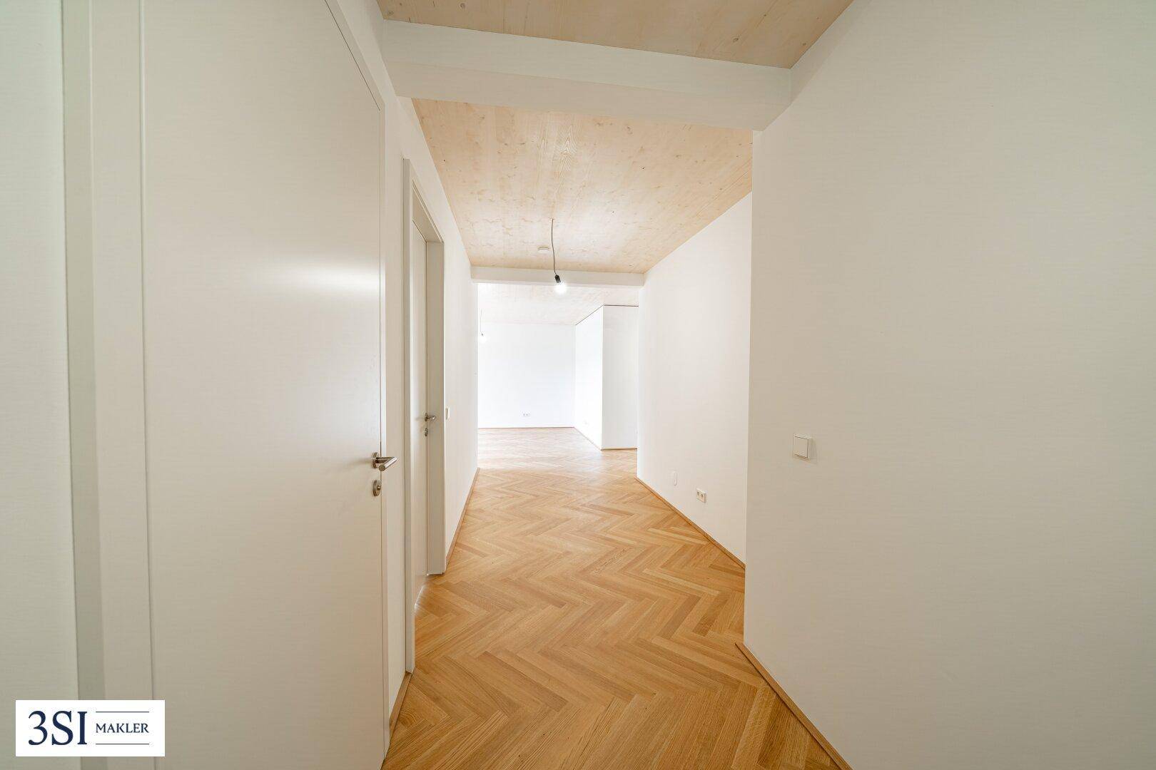 Heller Flur mit elegantem Fischgrätparkett und einer warmen Holzdecke, verbindet die verschiedenen Räume.