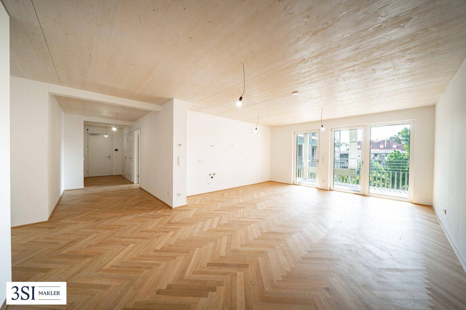 Weitläufiger Wohnbereich mit hellem Fischgrätparkett und Zugang zu einem Balkon, ideal für offene Gestaltungskonzepte.