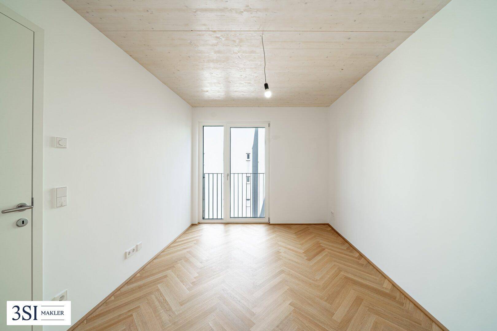 Geräumiges Schlafzimmer mit Fischgrätparkett und hohen Decken, bietet viel natürliches Licht durch die Balkontür.