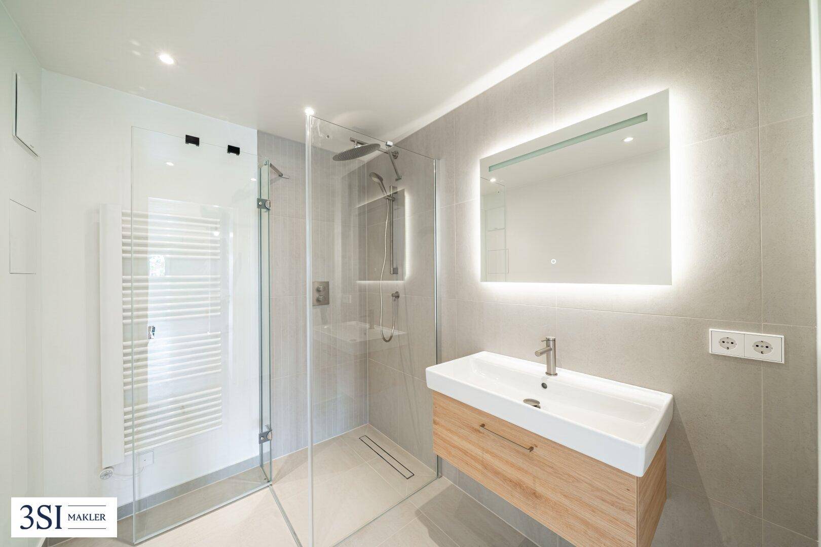 Modernes Badezimmer mit stilvollem Holzwaschtisch, beleuchtetem Spiegel und einer großzügigen Walk-in-Dusche.