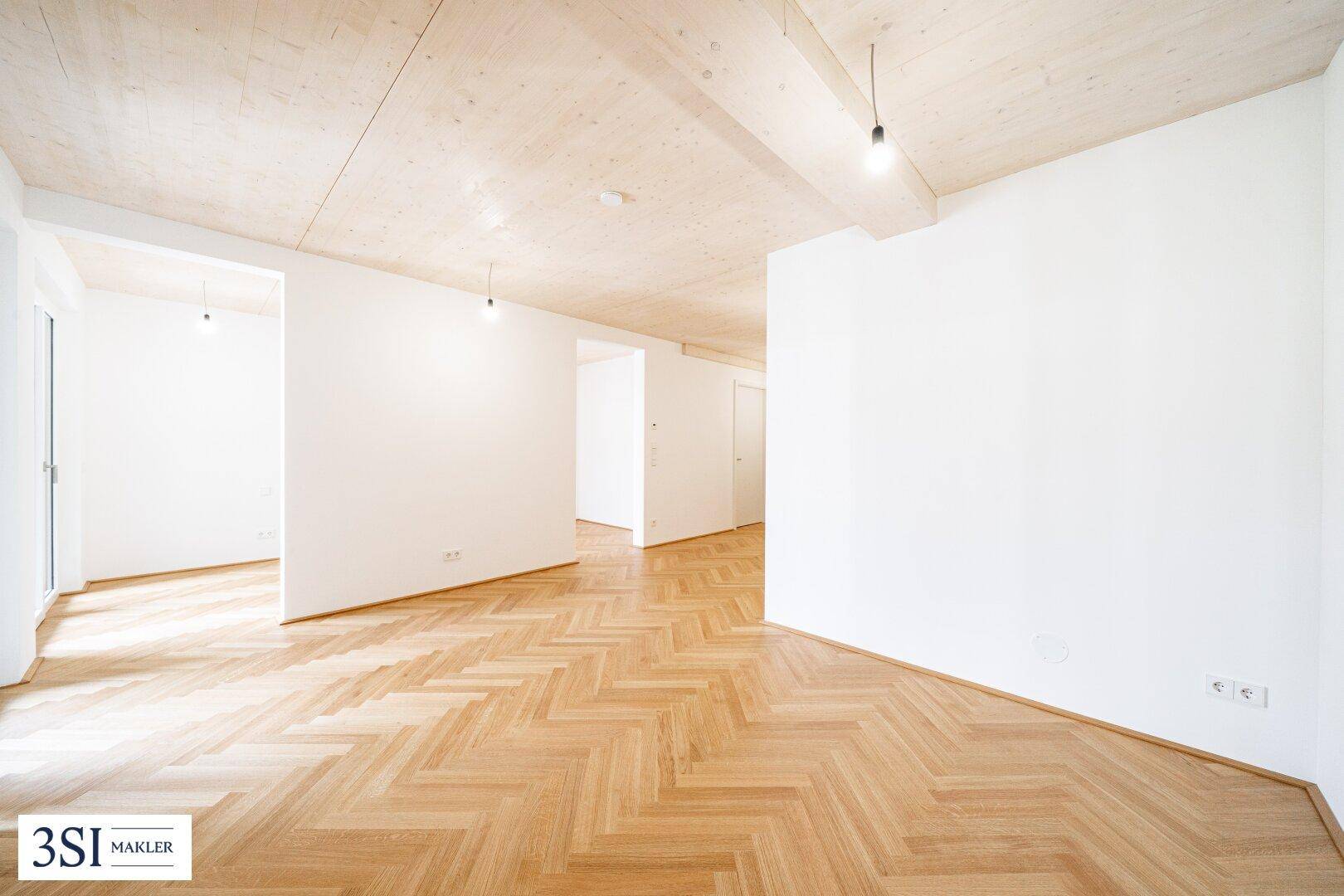 Offener Wohnbereich mit hellem Fischgrätparkett und sichtbaren Holzbalken an der Decke.