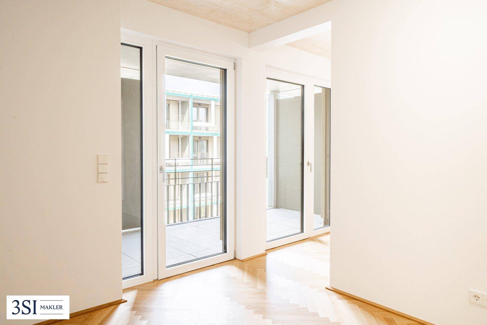 Heller Innenraum mit Fischgrätparkett und mehreren großen Fenstertüren zum Außenbereich.