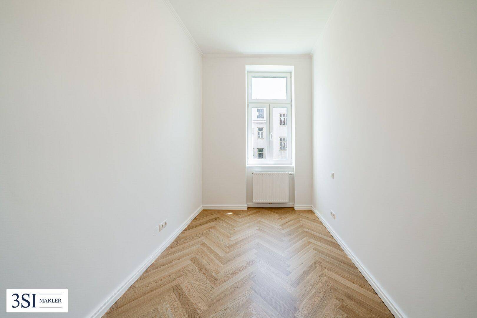 Kleiner, heller Raum mit Fischgrätparkett und einem Fenster, ideal als Schlaf- oder Arbeitszimmer.