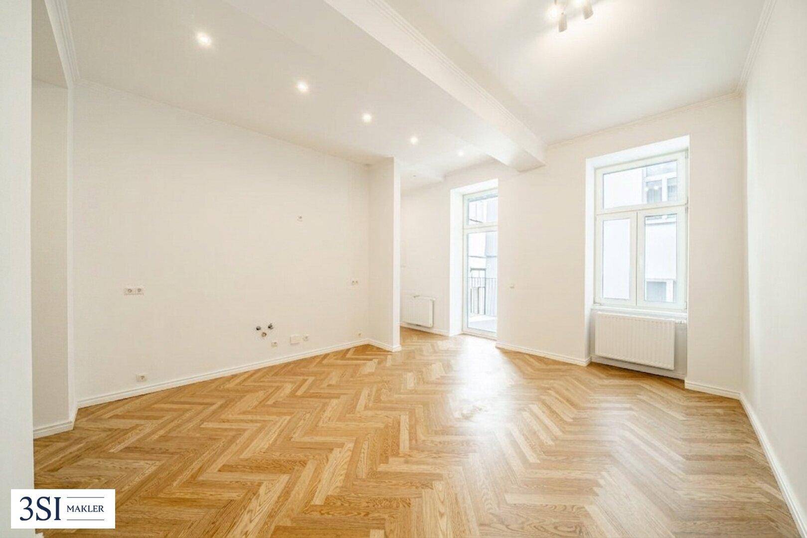 Geräumiger, unmöblierter Raum mit Fischgrätparkett und Zugang zu einem Balkon.