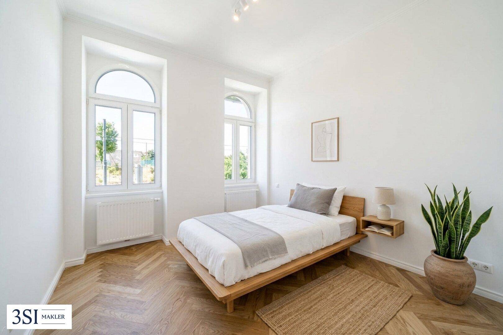 Schlafzimmer mit Fischgrätparkett, großen Fenstern und minimalistischer Einrichtung.