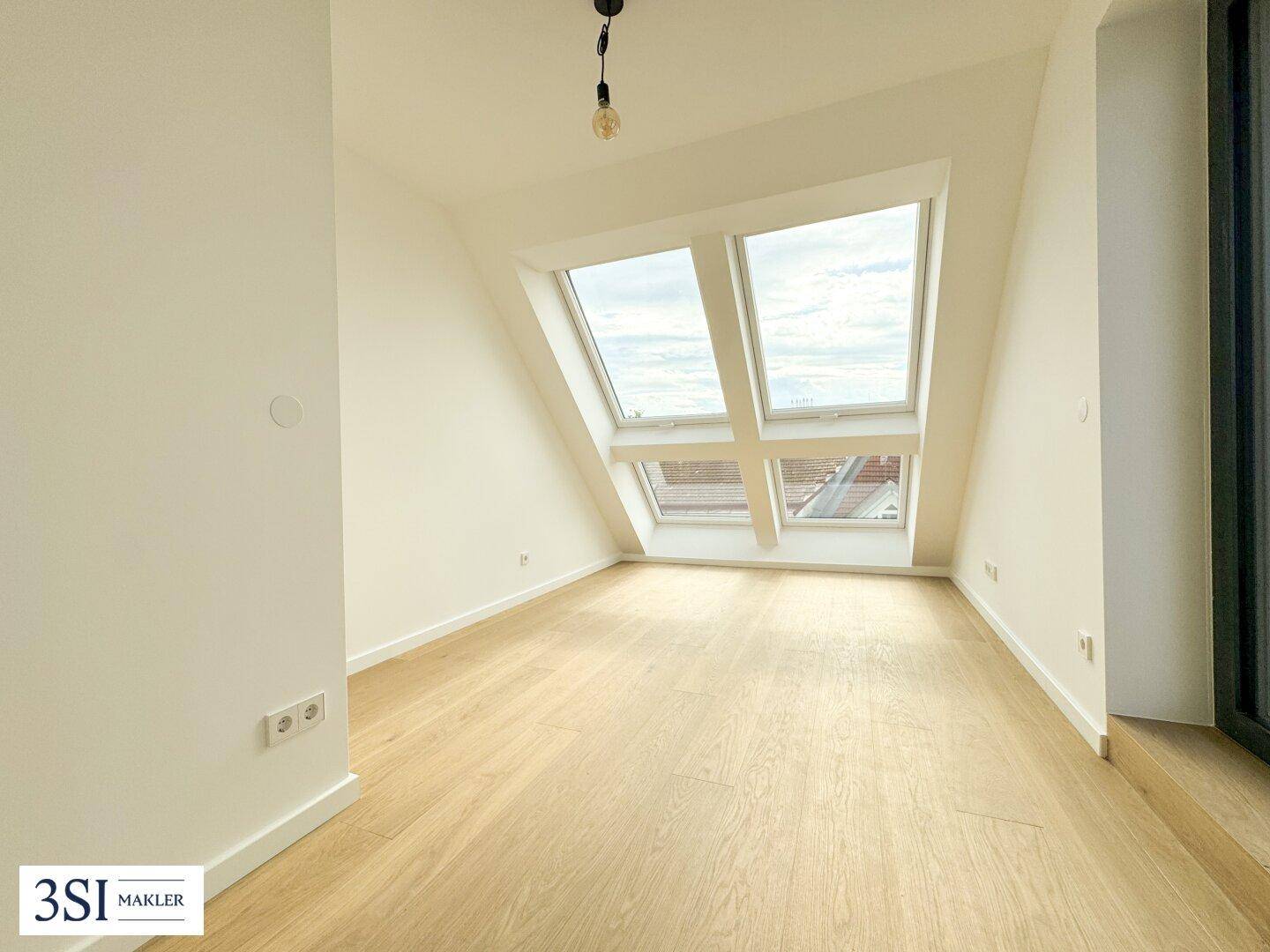 Geräumiger Raum mit Holzboden, Dachschrägen und zwei Dachfenstern, die für Helligkeit sorgen.