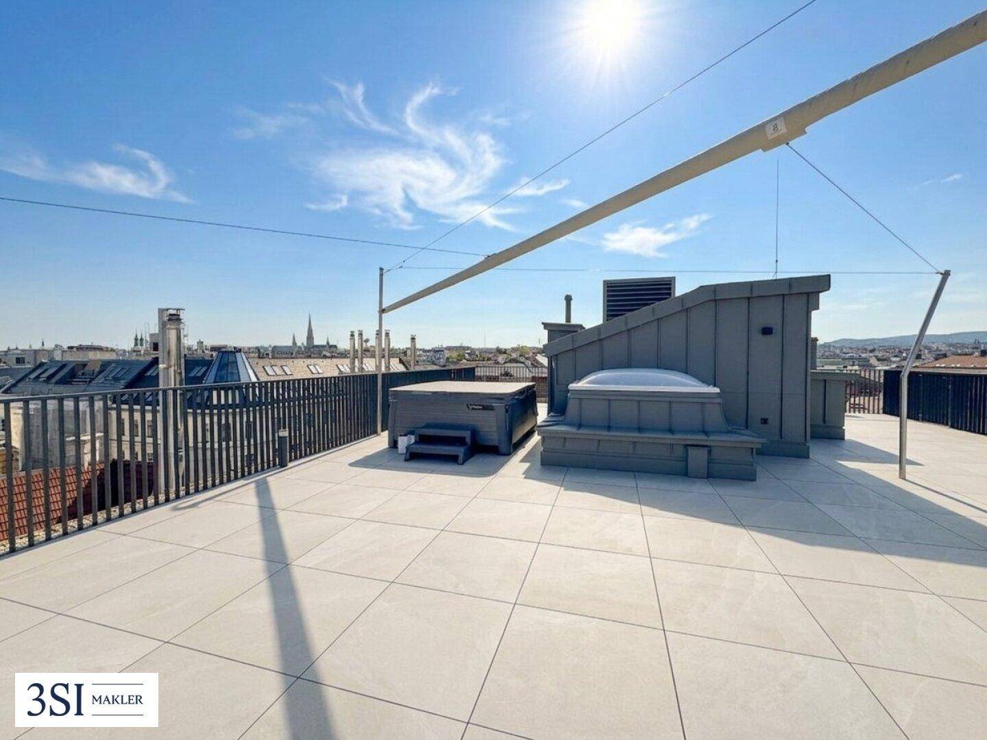 Großzügige Dachterrasse mit Whirlpool und weitem Blick über die Stadt unter blauem Himmel.
