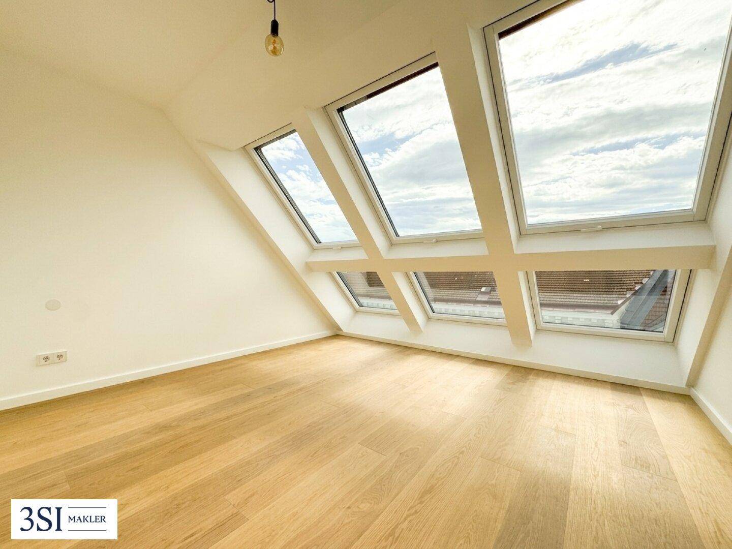 Heller Raum mit Holzboden, Dachschrägen und mehreren Dachfenstern, die viel Licht spenden.