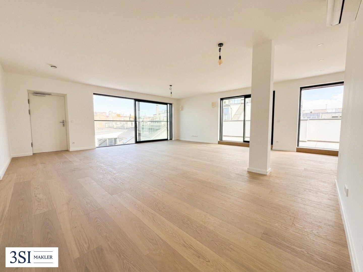 Heller, leerer Wohnbereich mit Holzboden und großen Fensterfronten, die viel Tageslicht hereinlassen.