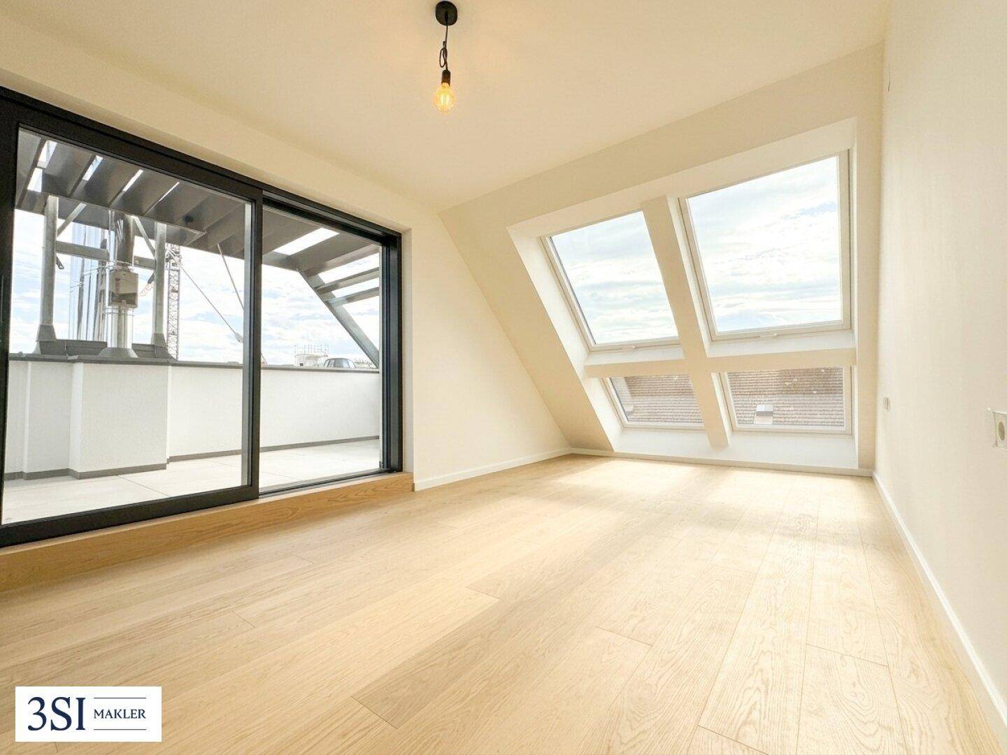 Heller Raum mit Holzboden, Dachschrägen, Dachfenstern und Zugang zu einem Balkon oder einer Terrasse.