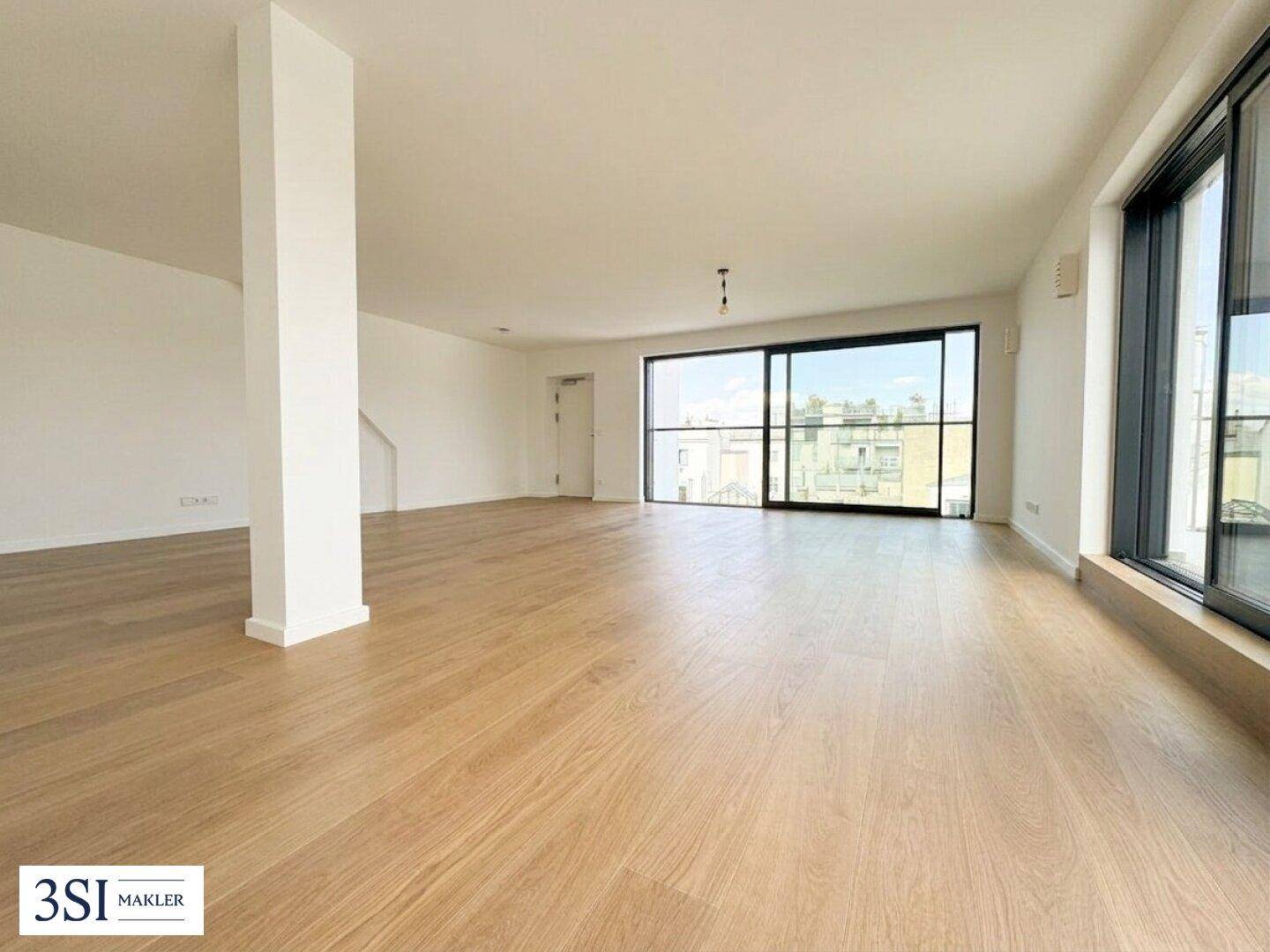 Geräumiges, leeres Wohnzimmer mit hellem Holzboden und großen Schiebetüren zur Terrasse.