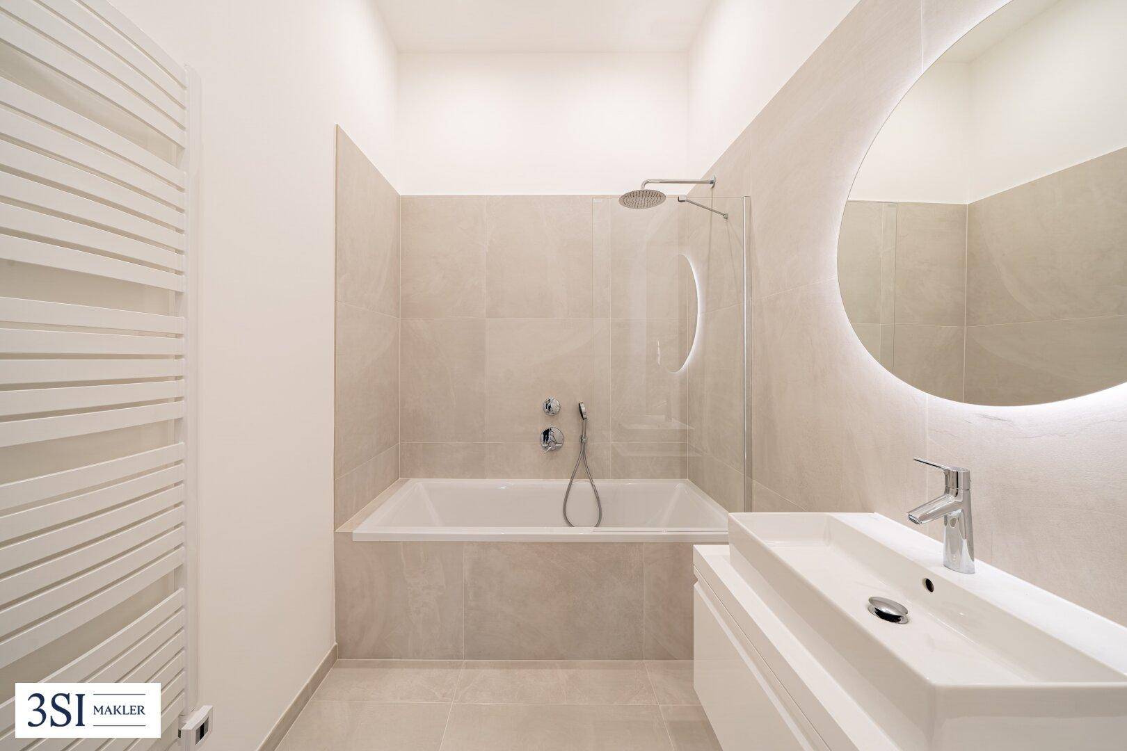 Modernes Badezimmer mit Badewanne, Regendusche, beheiztem Handtuchhalter und beleuchtetem Spiegel.