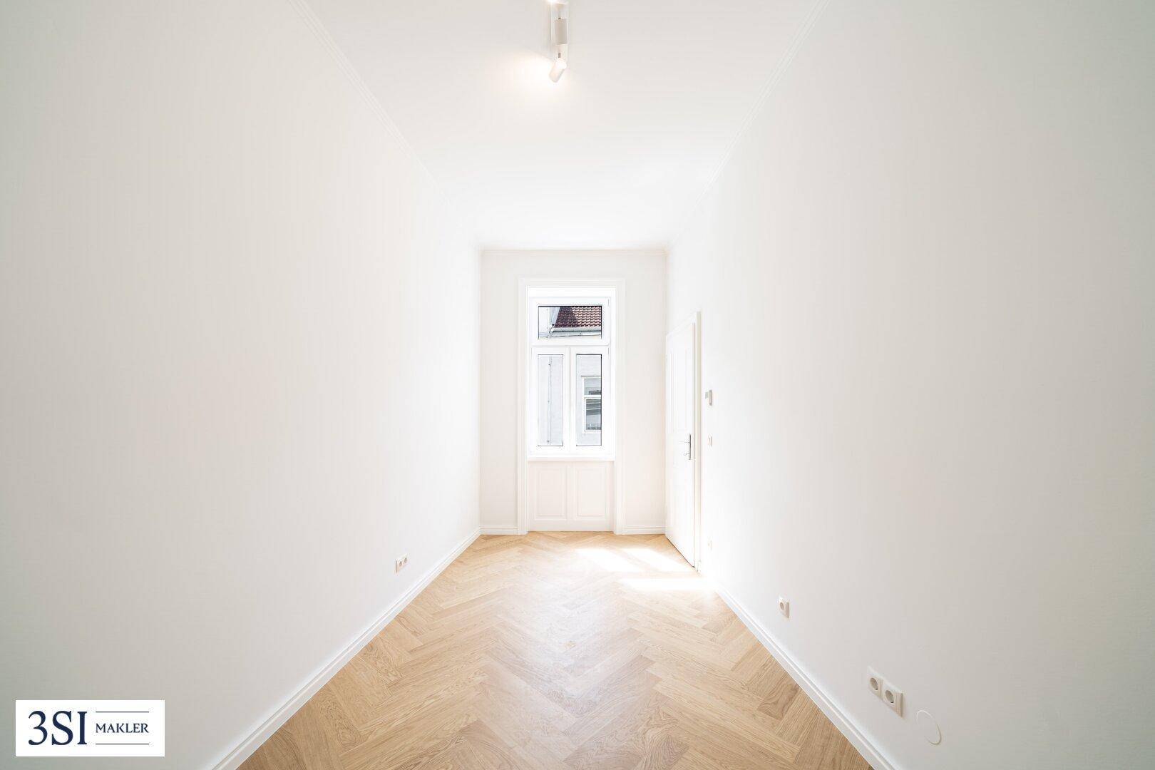 Schmaler, heller Raum mit Fischgrätparkett und einem Fenster, geeignet als Schlaf- oder Arbeitszimmer.