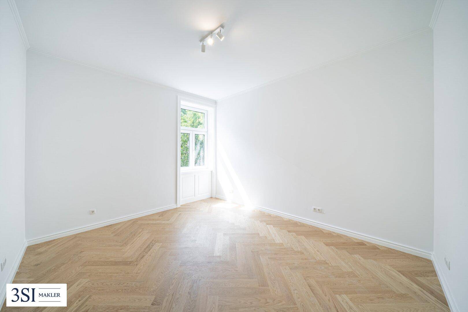 Geräumiges Zimmer mit hellem Fischgrätparkett und zwei großen Fenstern, frisch renoviert.