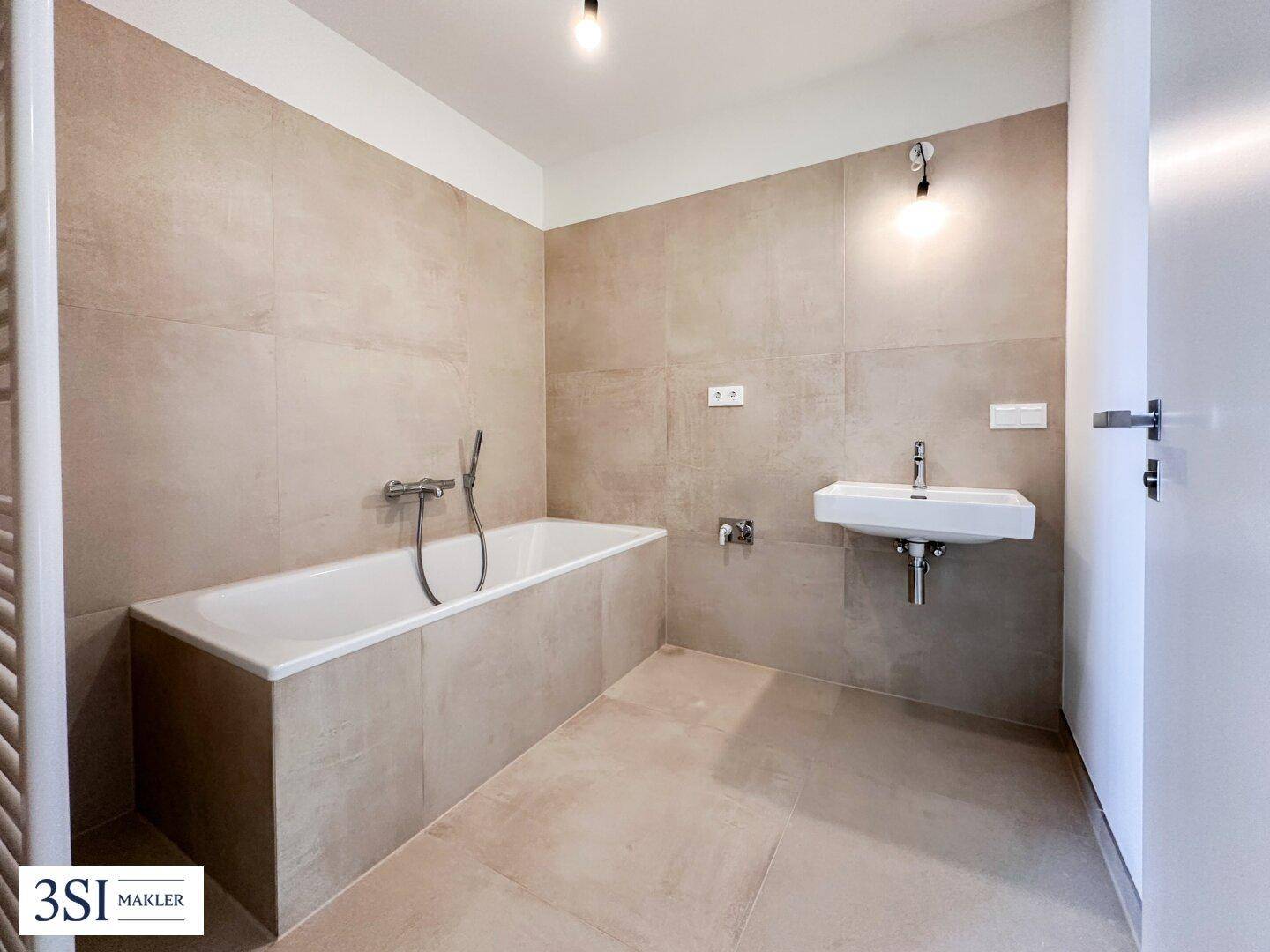 Modernes Badezimmer mit Badewanne, Einzelwaschbecken und beigefarbenen Fliesen, inklusive Handtuchheizkörper.