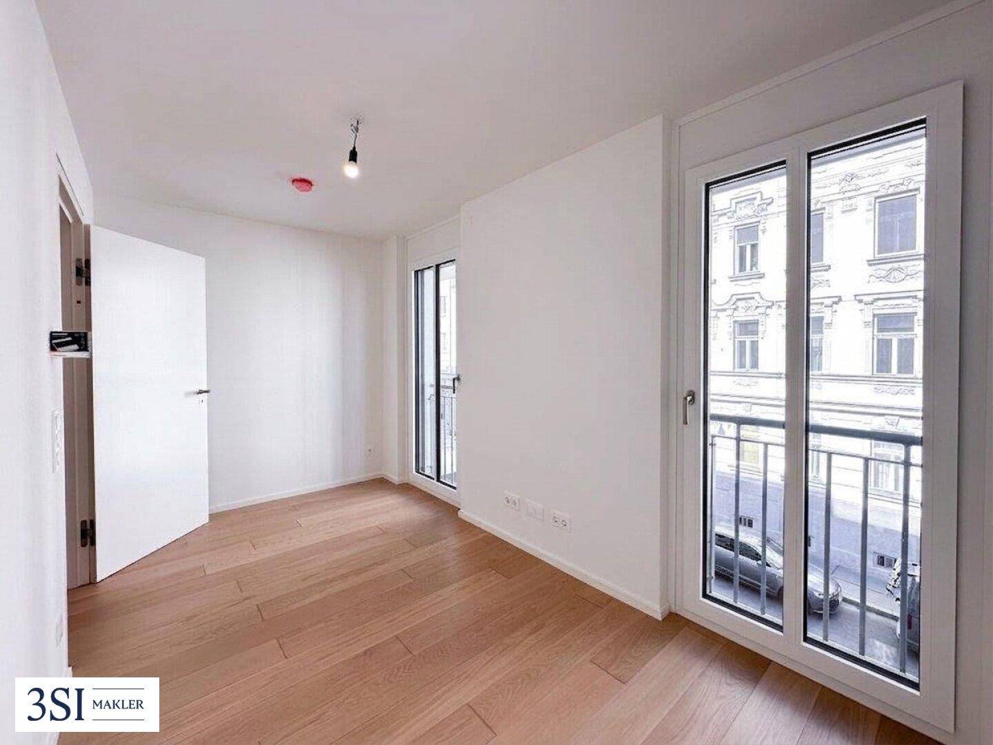 Helles Zimmer mit Holzboden und zwei französischen Balkonen, die einen Blick auf die Straße bieten.