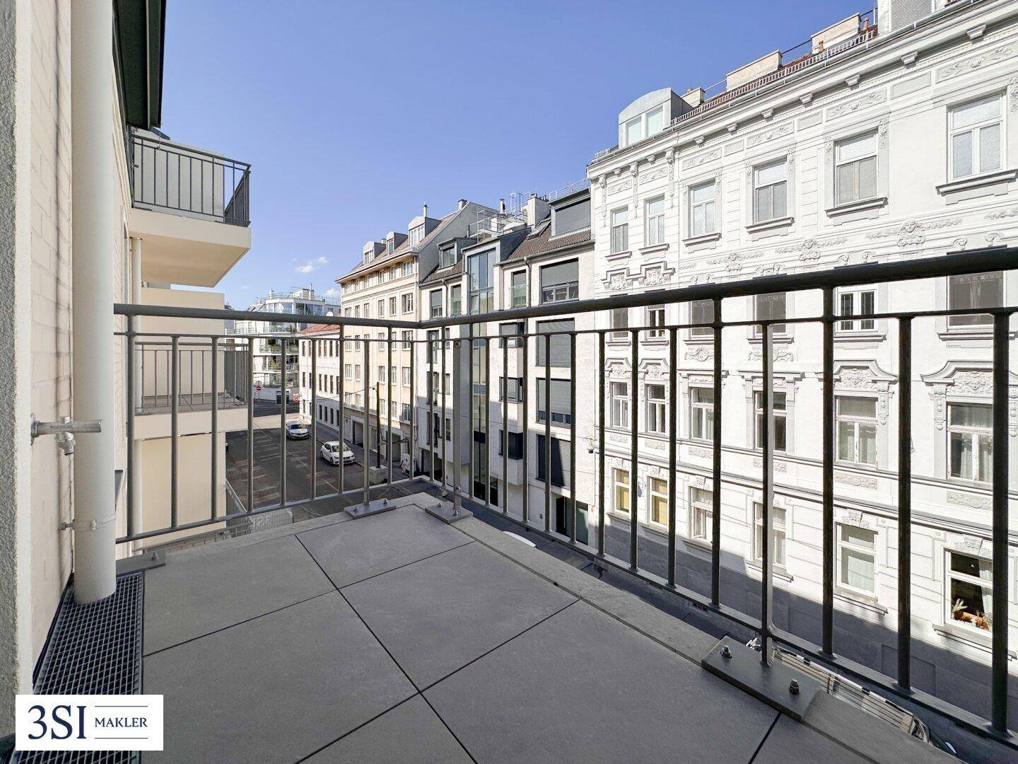 Geräumiger Balkon mit Blick auf die umliegenden Stadtgebäude und viel Tageslicht.
