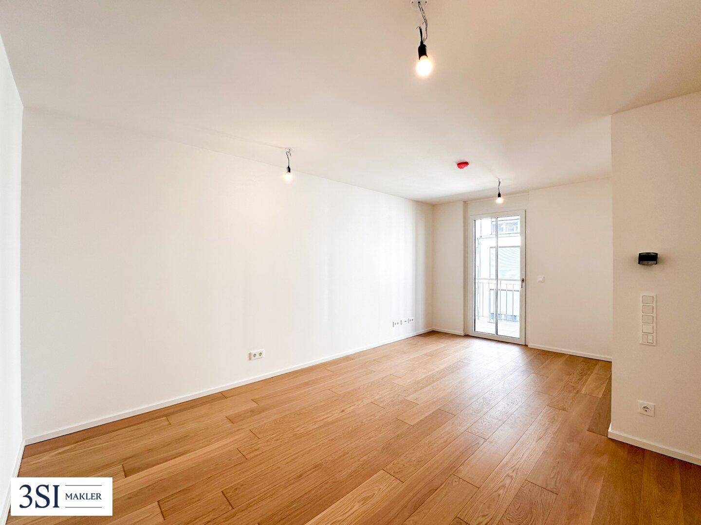 Lichtdurchfluteter Raum mit Holzboden und Tür zum Außenbereich, ideal als Wohnzimmer.