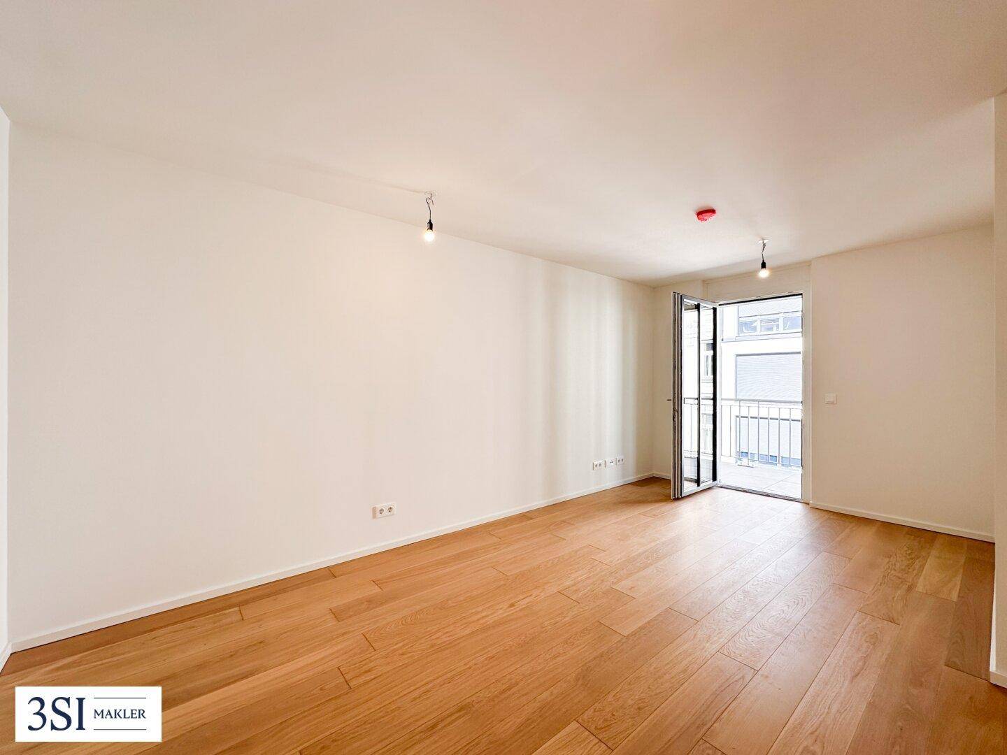 Heller Wohnraum mit Eichenparkettboden und Zugang zu einem Balkon.