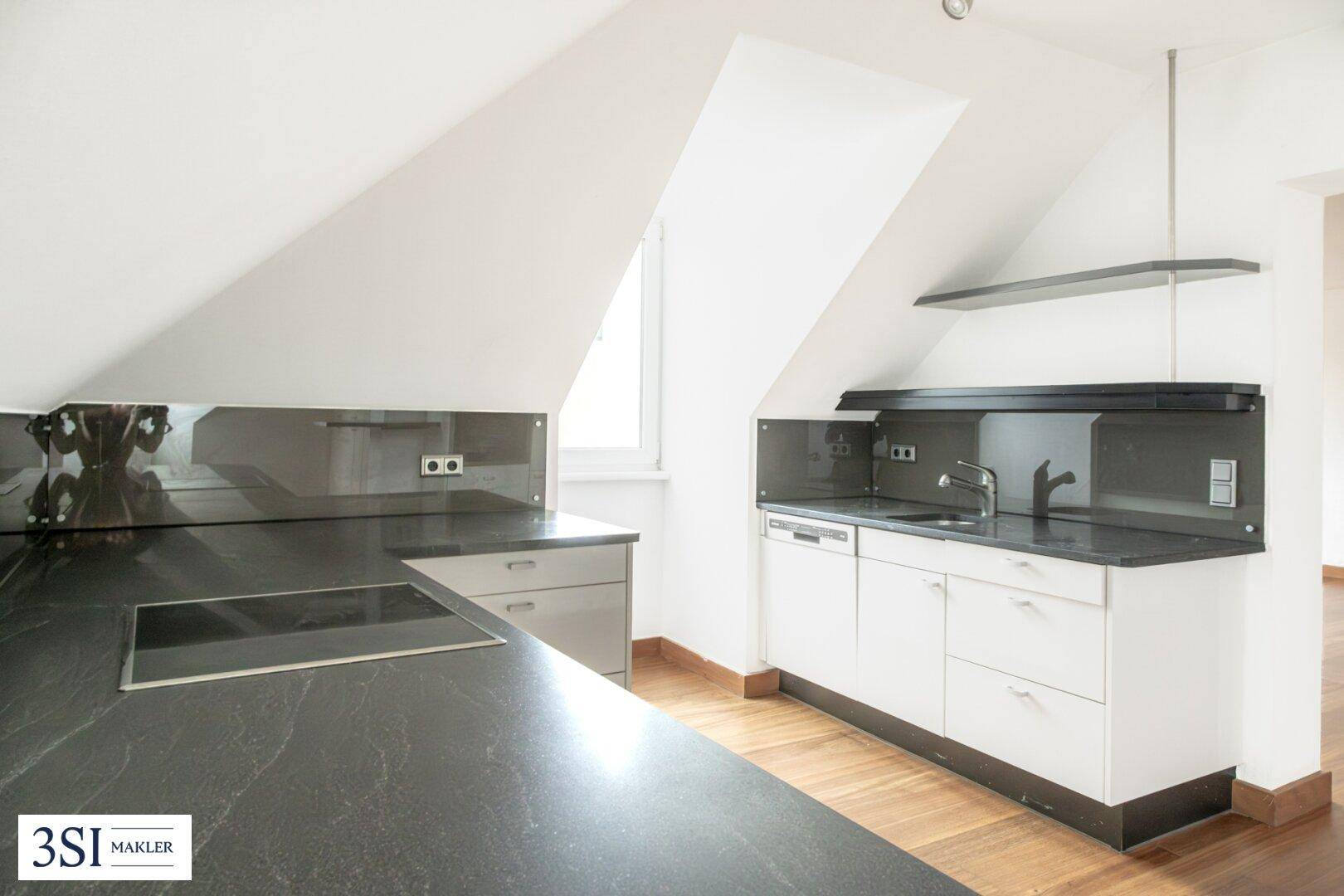 Moderne Küche mit dunklen Arbeitsplatten, weißen Schränken und Induktionskochfeld unter Dachschräge.