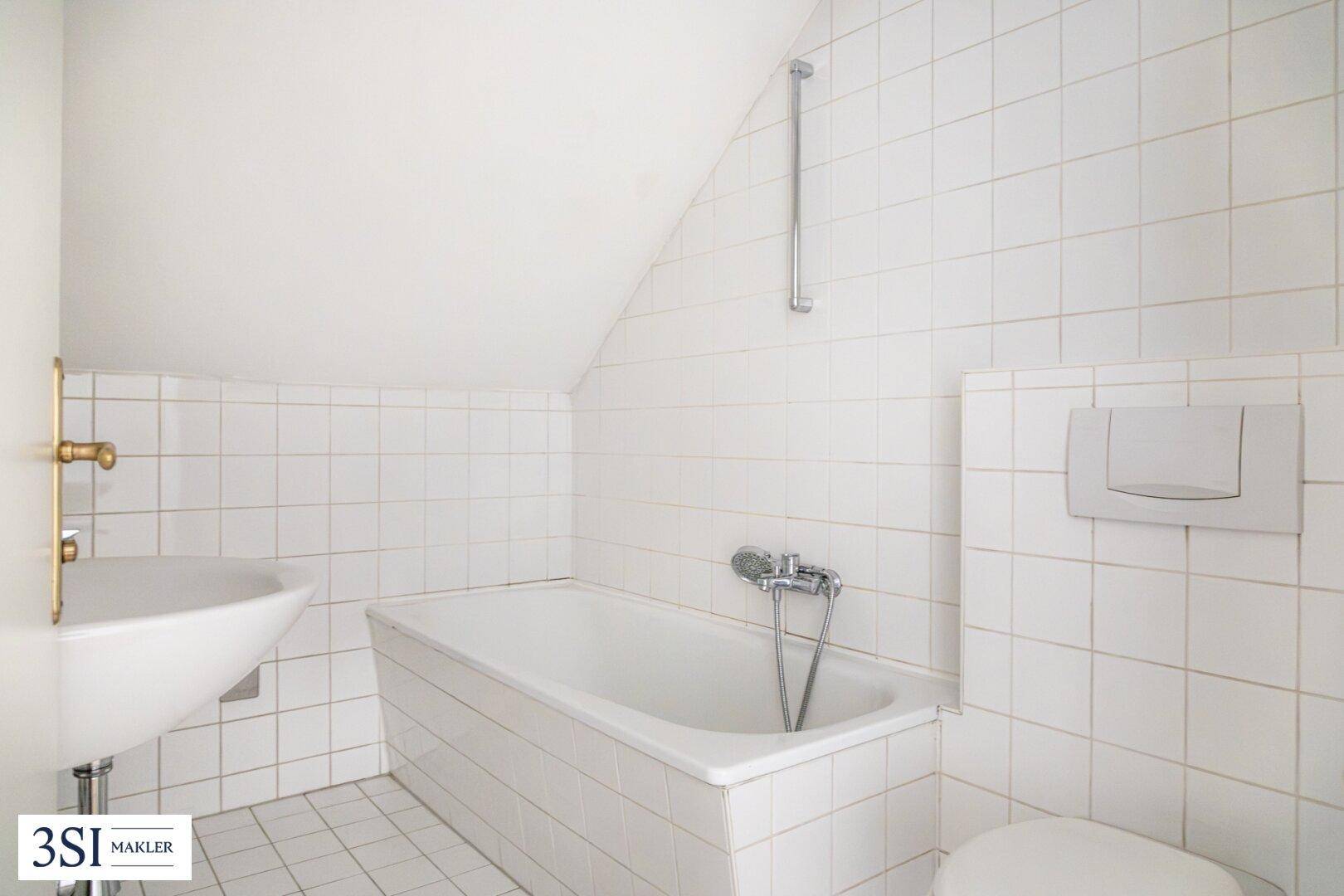 Badezimmer im Dachgeschoss mit Badewanne, WC und weißen Fliesen.