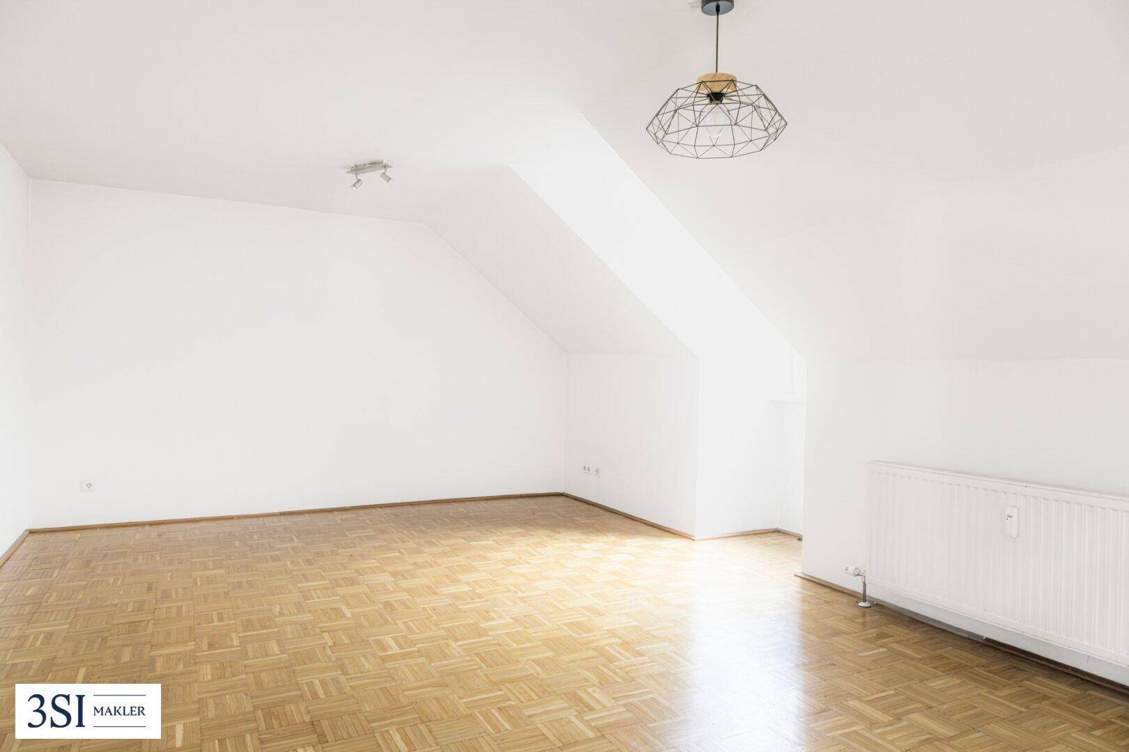 Geräumiger Wohnbereich im Dachgeschoss mit hellem Parkettboden und Schrägen.