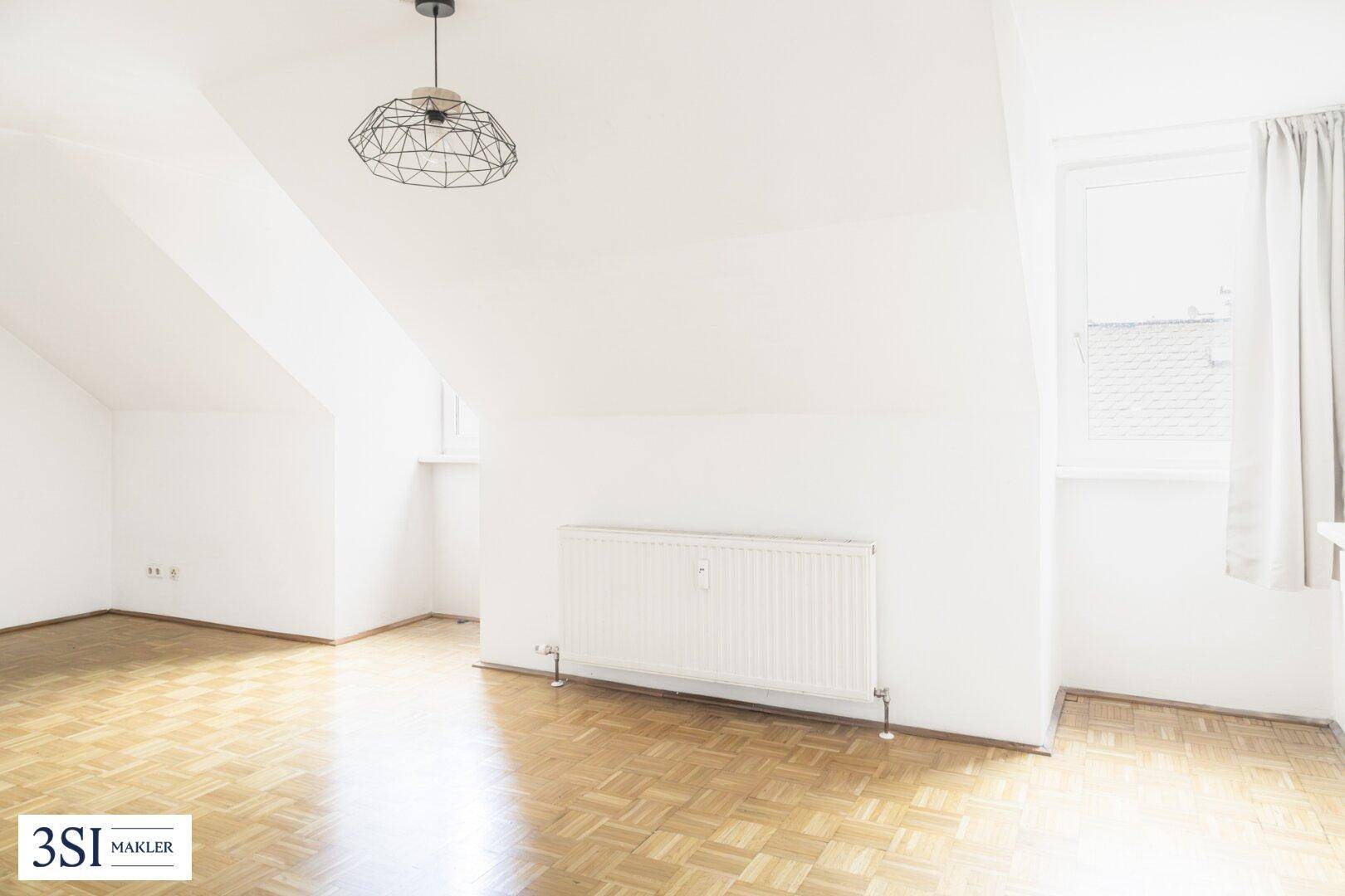 Heller Dachgeschossraum mit Fenster, Heizkörper und Parkettboden.