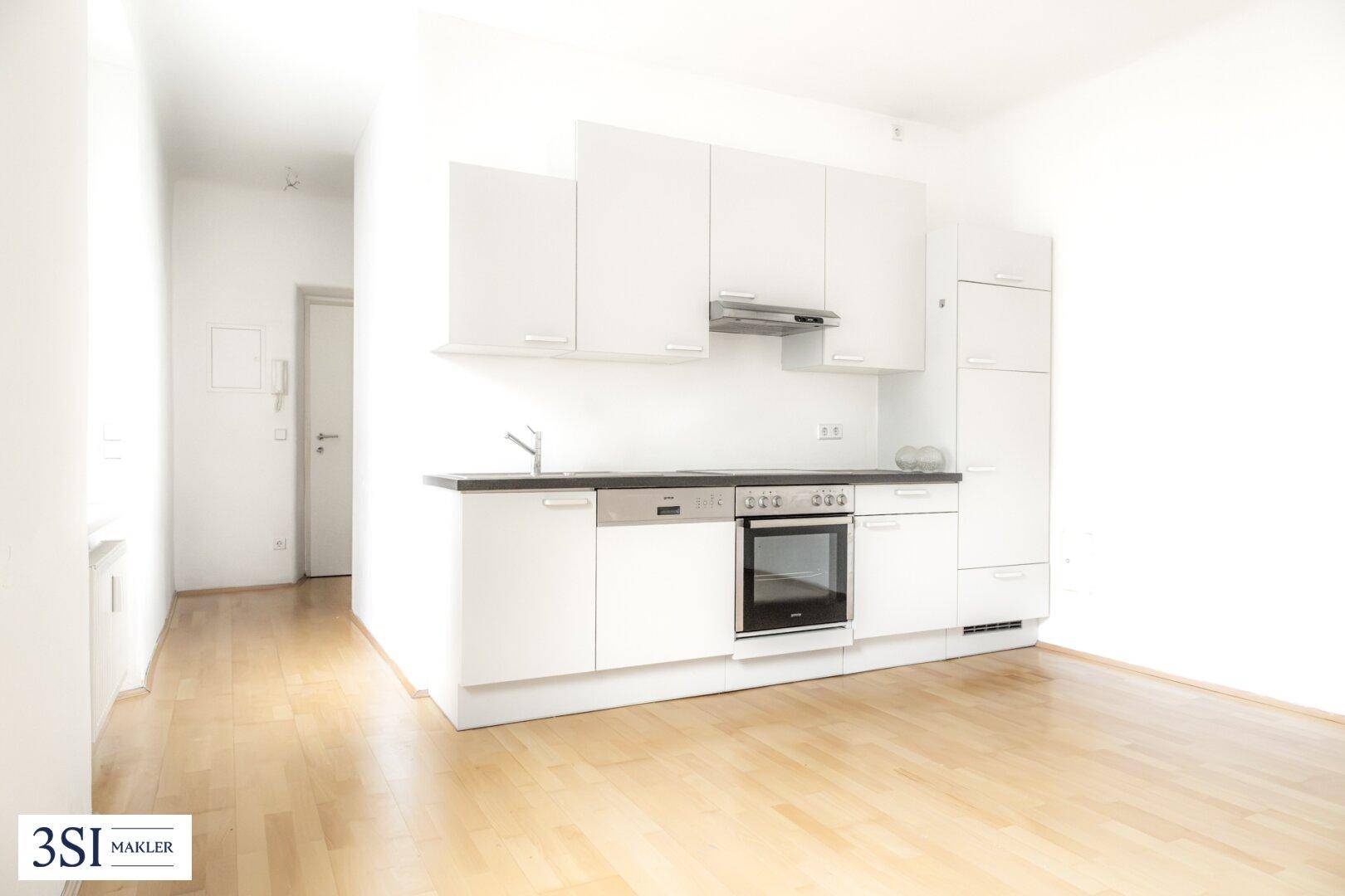 Moderne weiße Einbauküche mit Holzparkett und Zugang zum Flur.