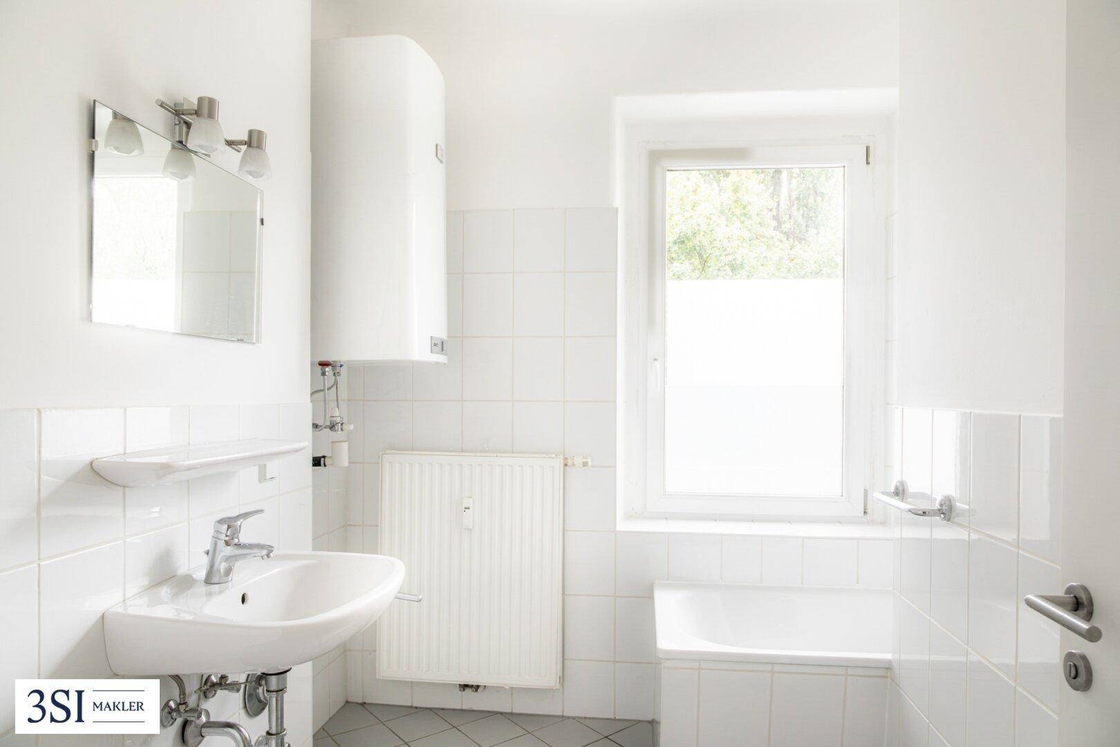 Weiß gefliestes Badezimmer mit Badewanne, Waschbecken und Fenster für natürliches Licht.