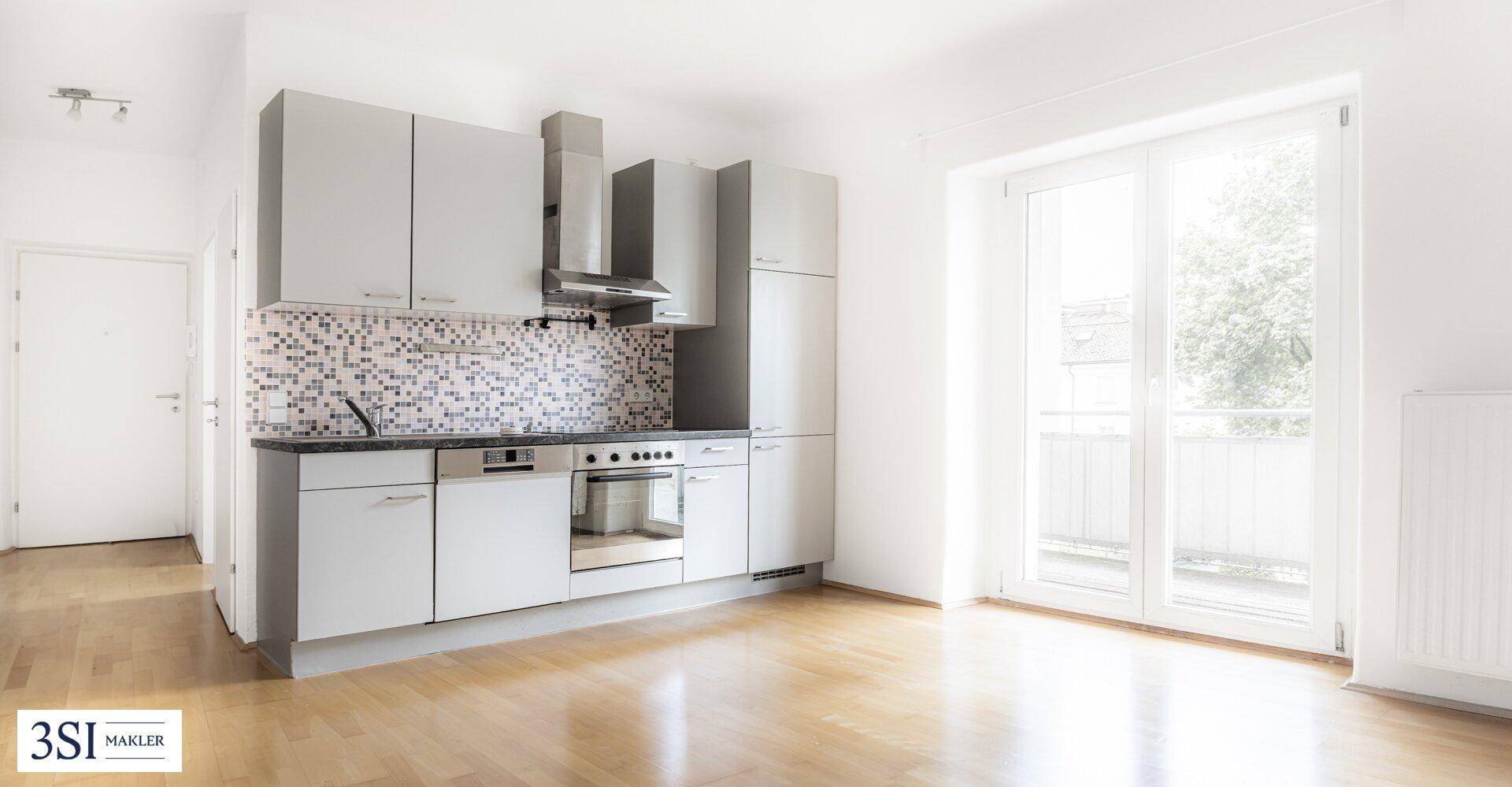 Helle Küche mit grauen Schränken, Mosaikfliesen und Zugang zu einem Balkon.