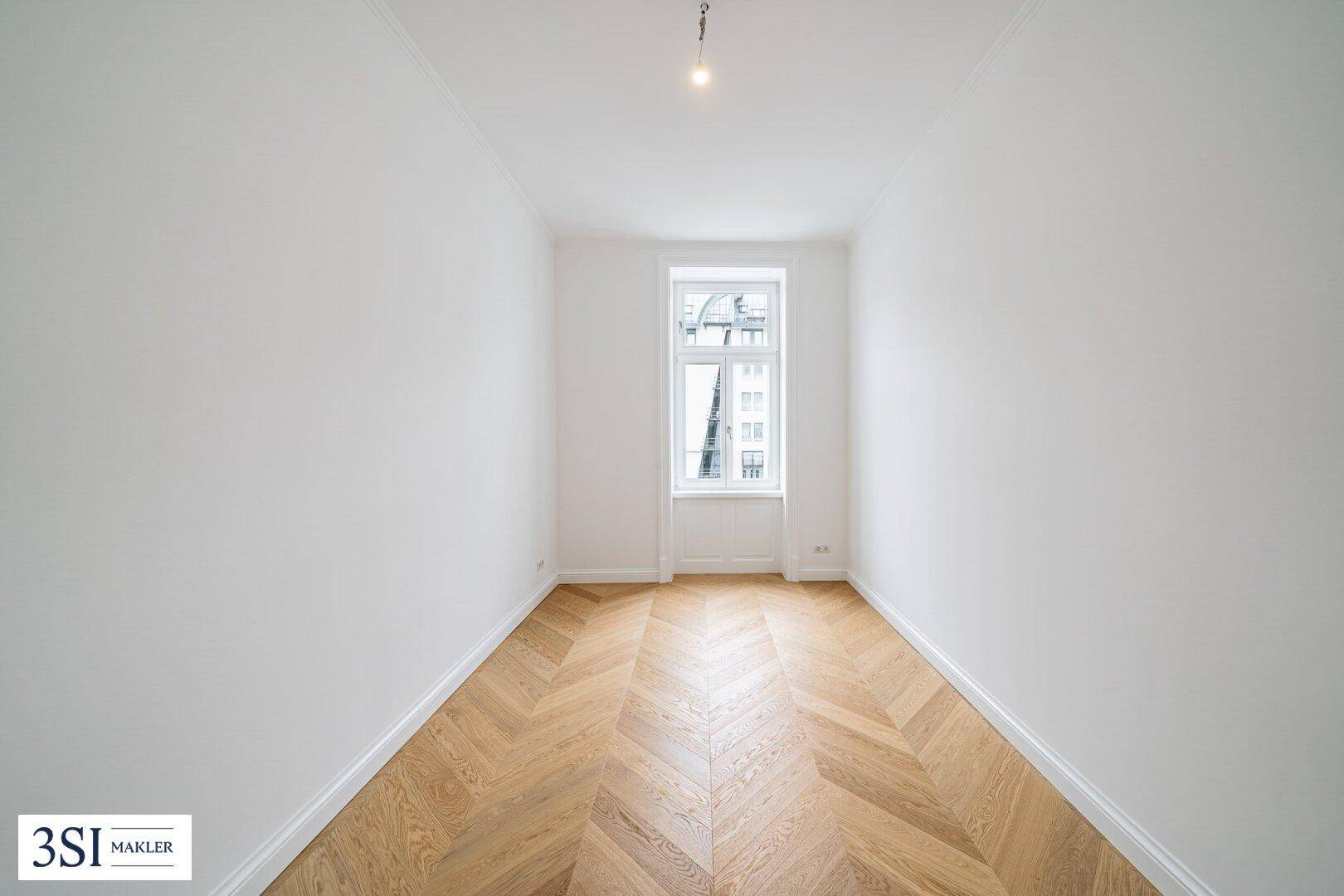 Schmaler, heller Raum mit Fischgrätparkett und einem hohen Fenster oder Tür.