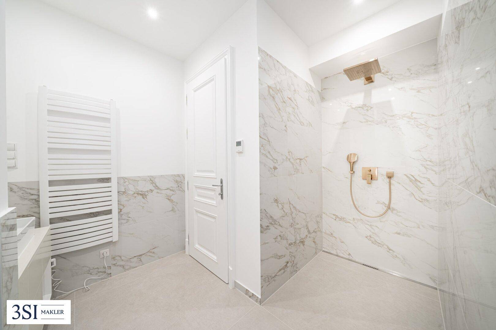 Modernes Badezimmer mit Marmoroptik-Fliesen, ebenerdiger Dusche und goldenen Armaturen.